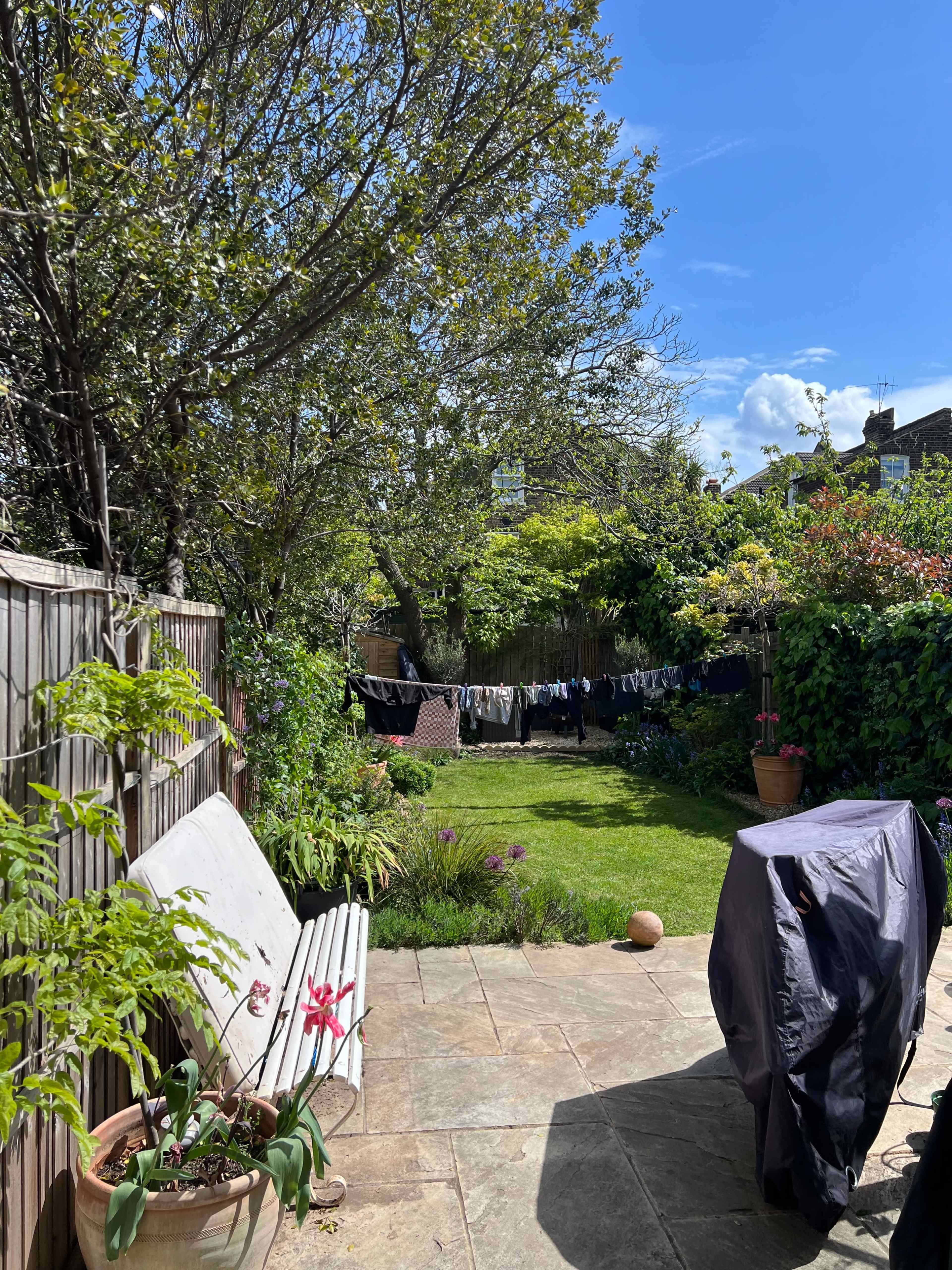 The image shows a garden with a grassy area, a stone patio, and clothes hanging on a line in the background.