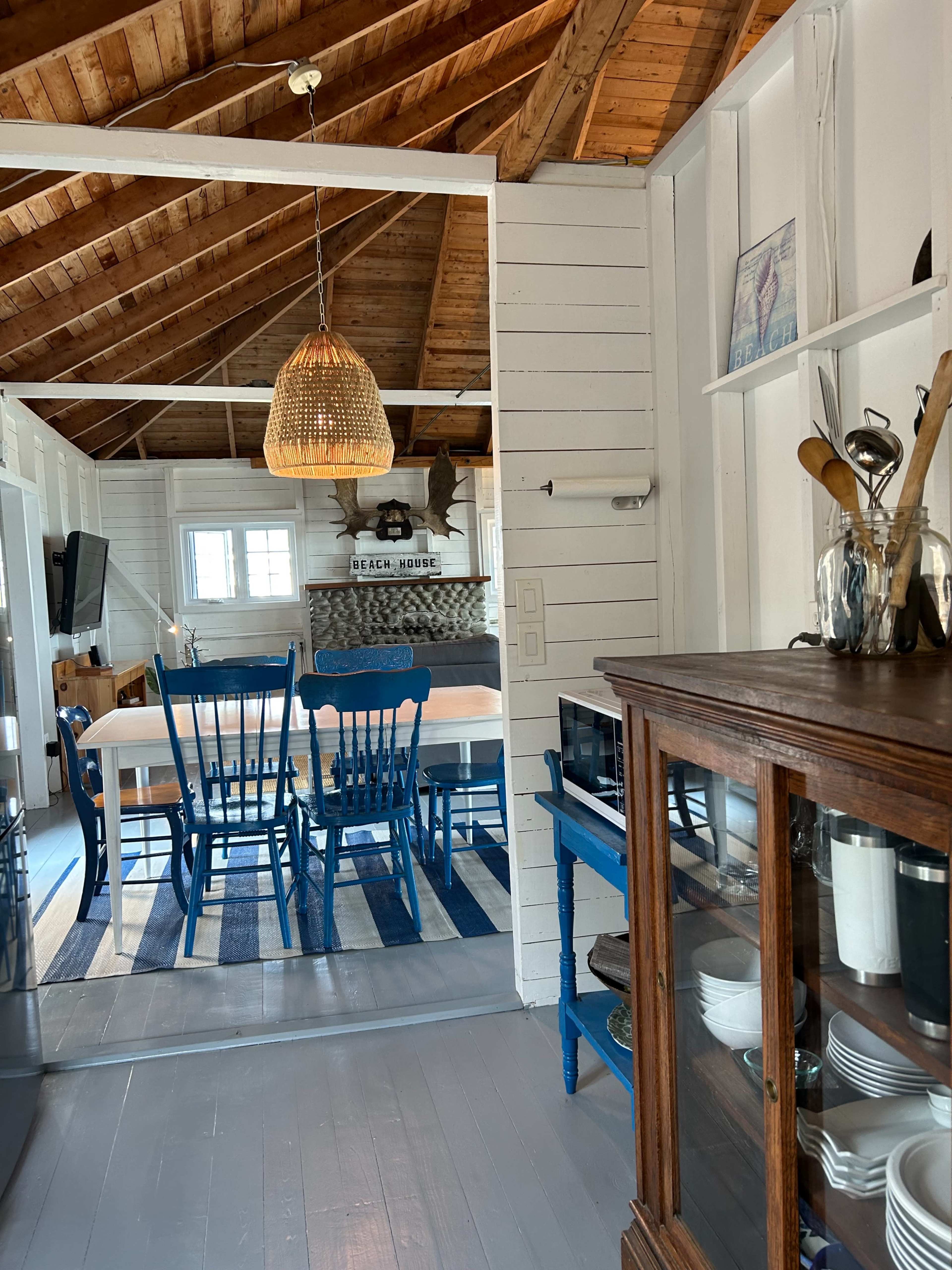A spacious, well-lit kitchen features a dining area with a wooden table and blue chairs, visible through a mirrored partition.
