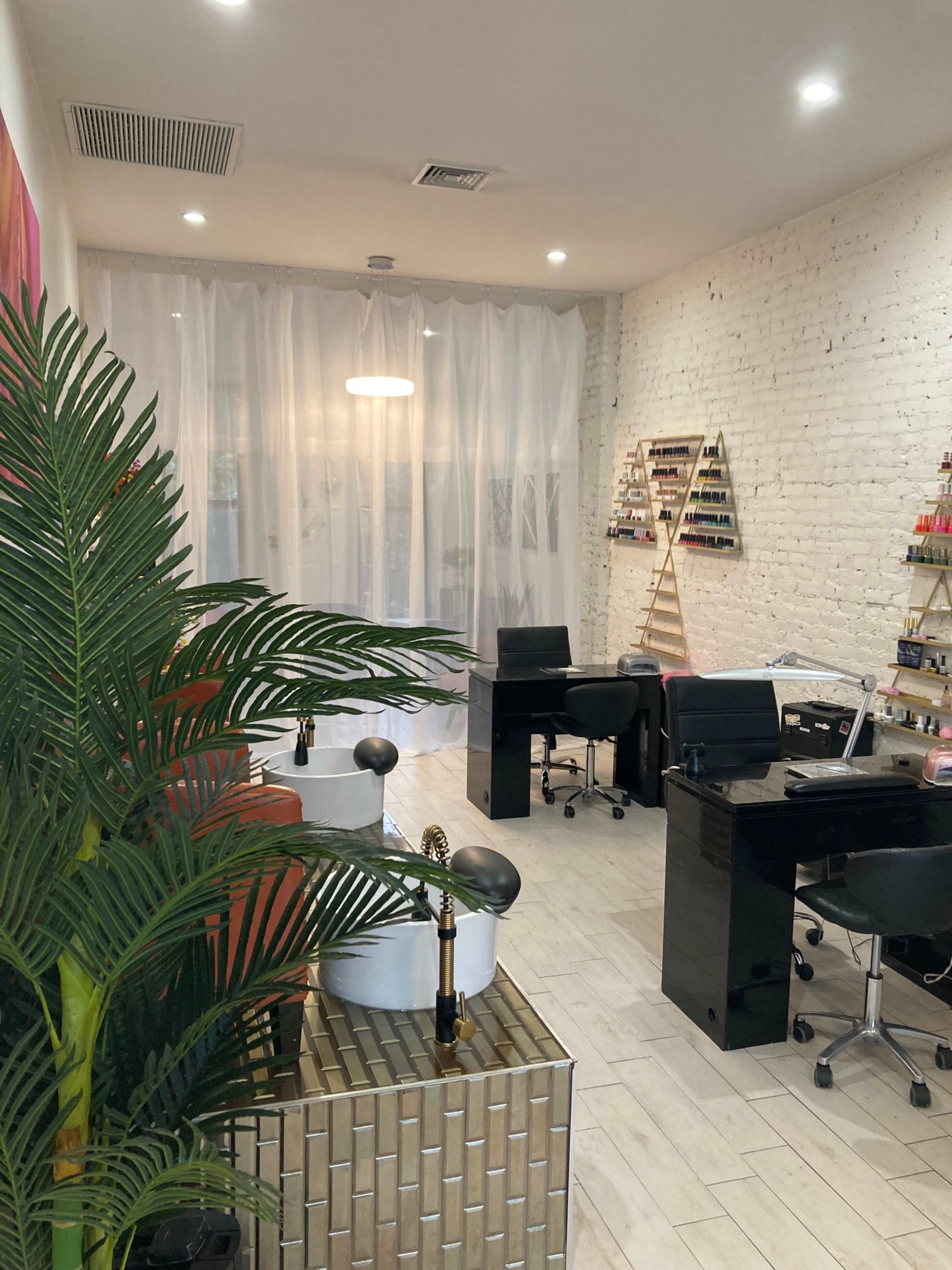 The image shows a well-organized beauty salon with a white brick wall, sleek black furniture, and a decorative plant in the foreground.