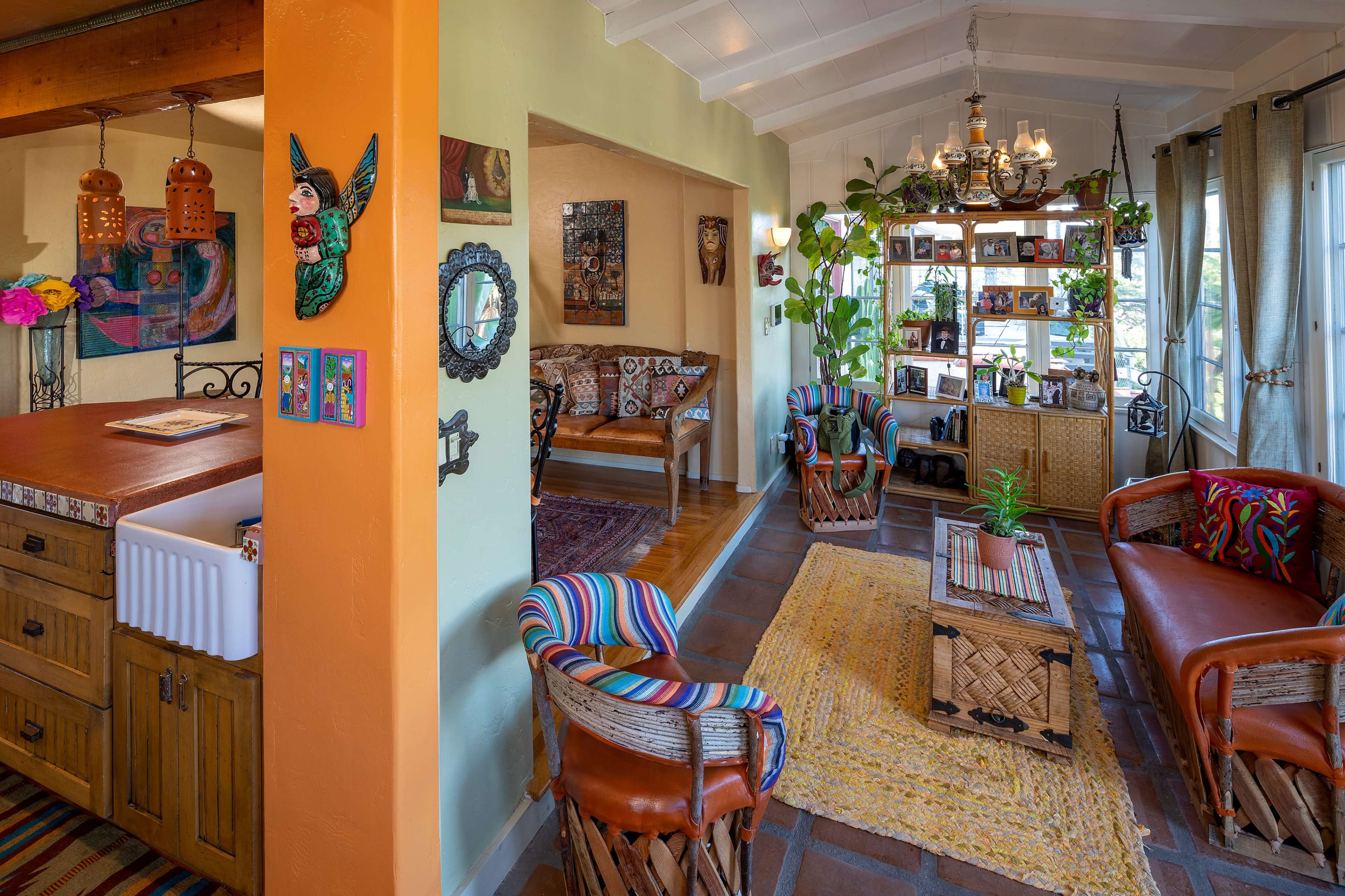 A brightly decorated living space with a cozy seating area, a wooden kitchen bar, and various plants and artwork adorning the walls.