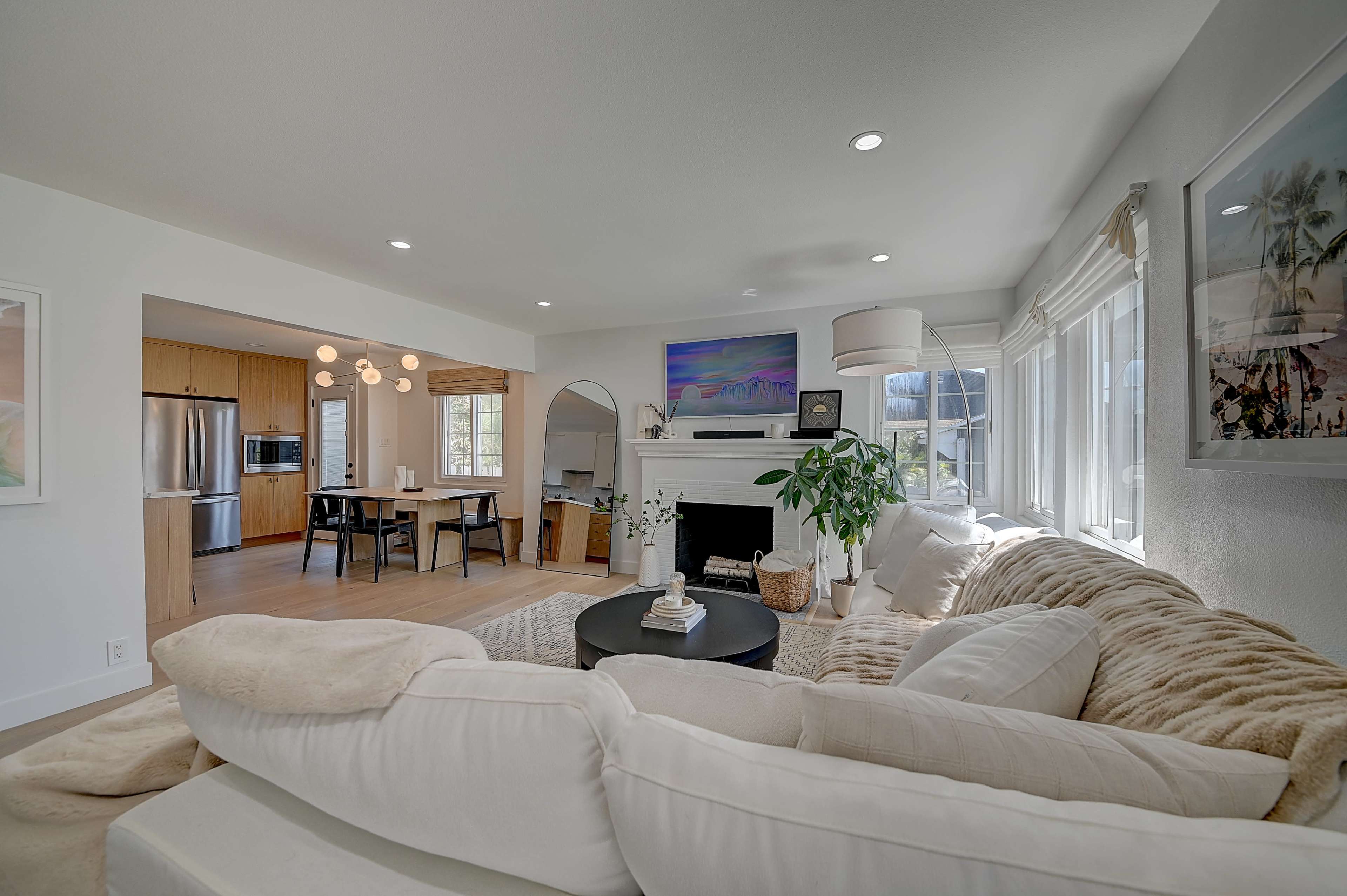 A modern, open-concept living room with a large sectional sofa, a coffee table, and a view into a dining and kitchen area with a dining table and appliances.