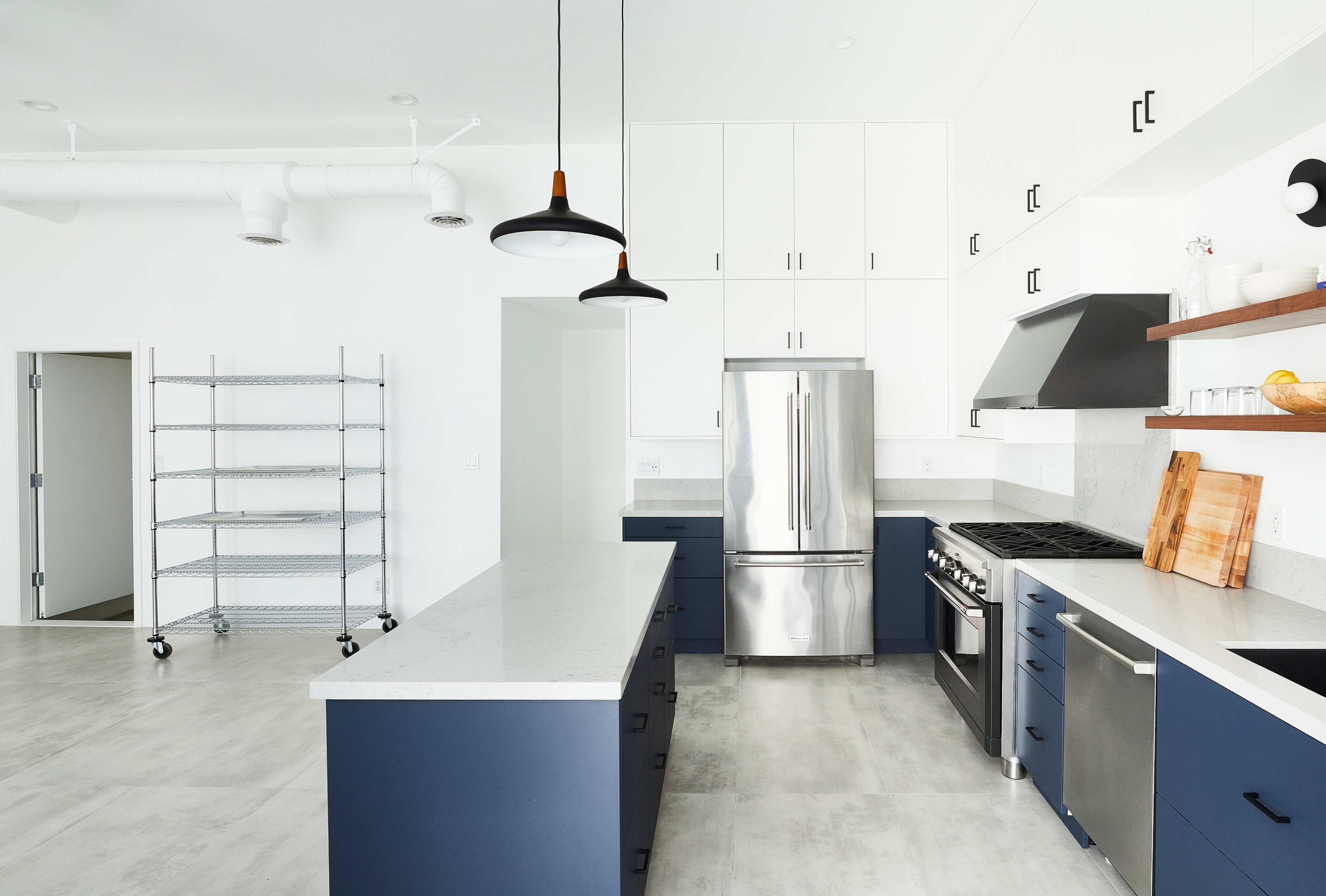 A modern kitchen features a stainless steel refrigerator, a gas range, and a central island with dark blue cabinetry.