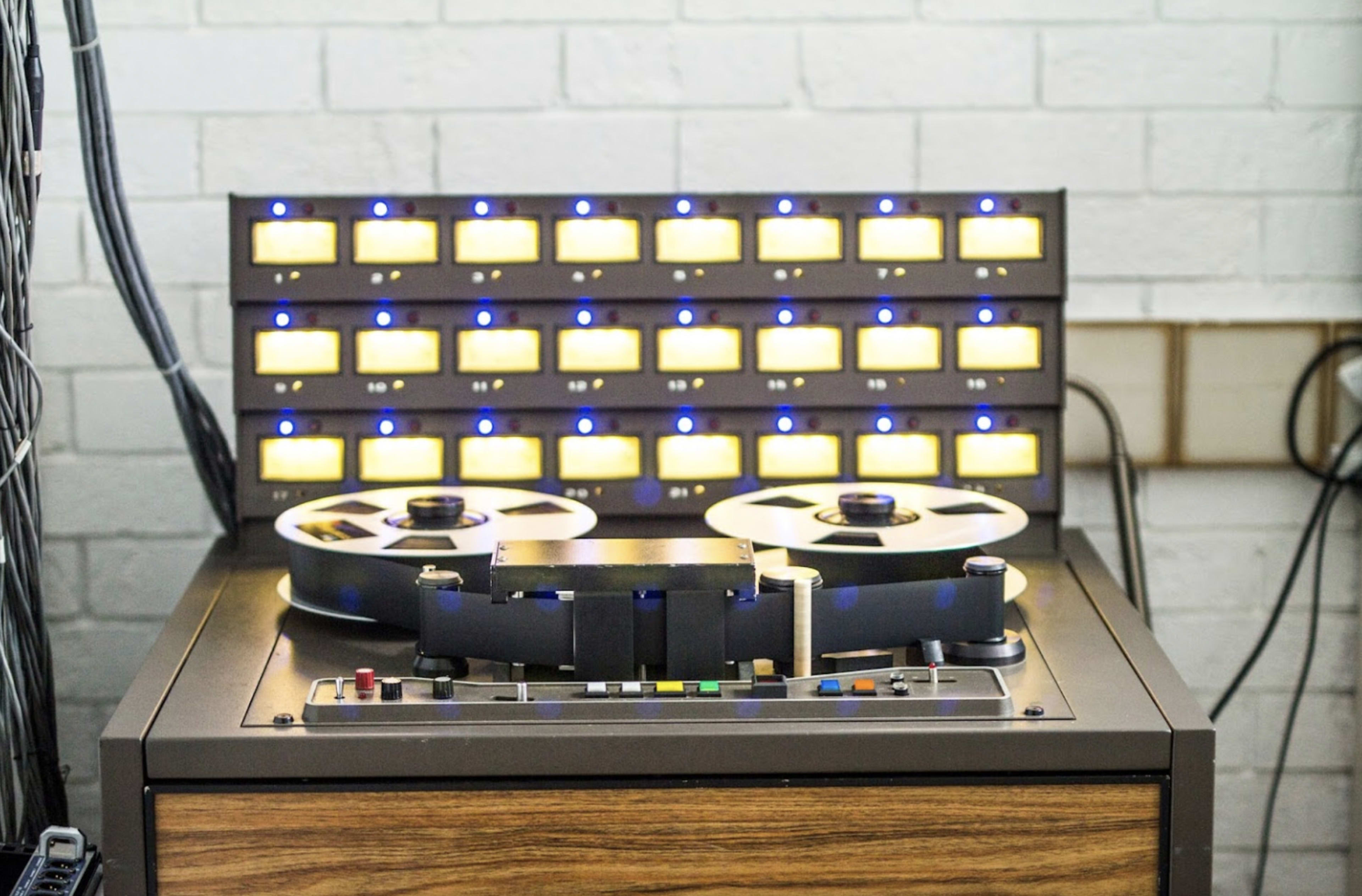 A vintage reel-to-reel tape recorder with illuminated control buttons and reels mounted on a wooden cabinet.