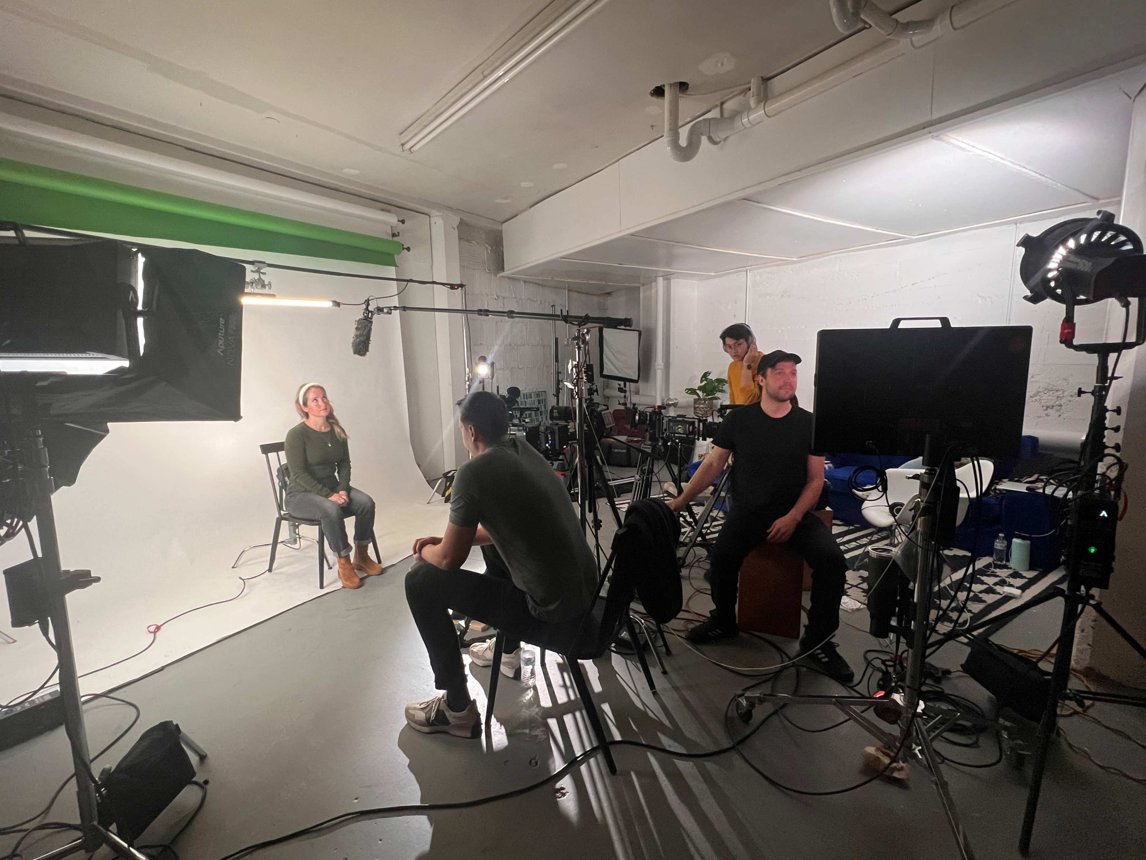 A film crew is recording an interview in a studio equipped with lights, cameras, and sound equipment.