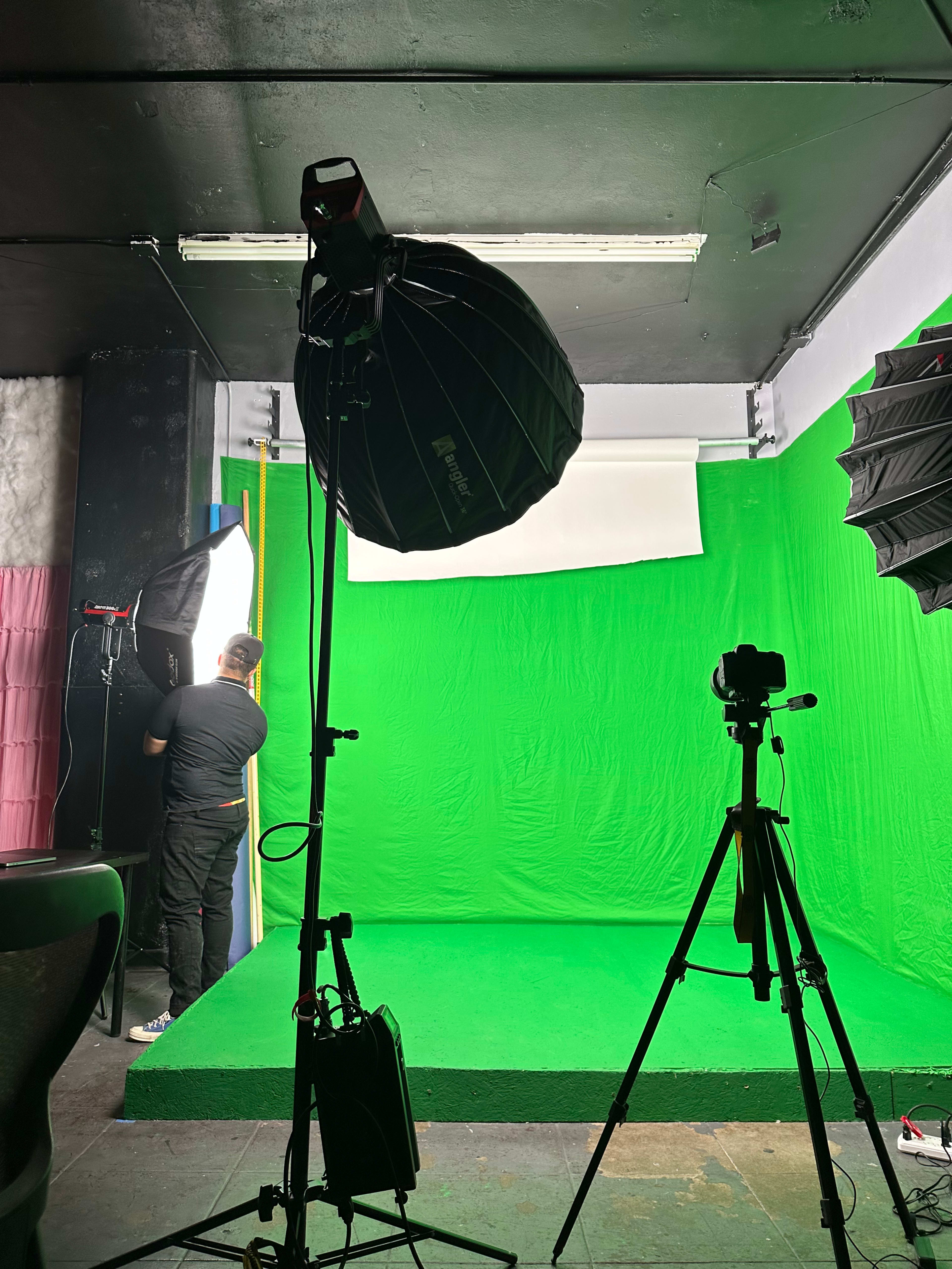 A green screen studio is set up with lighting equipment and a camera on a tripod.