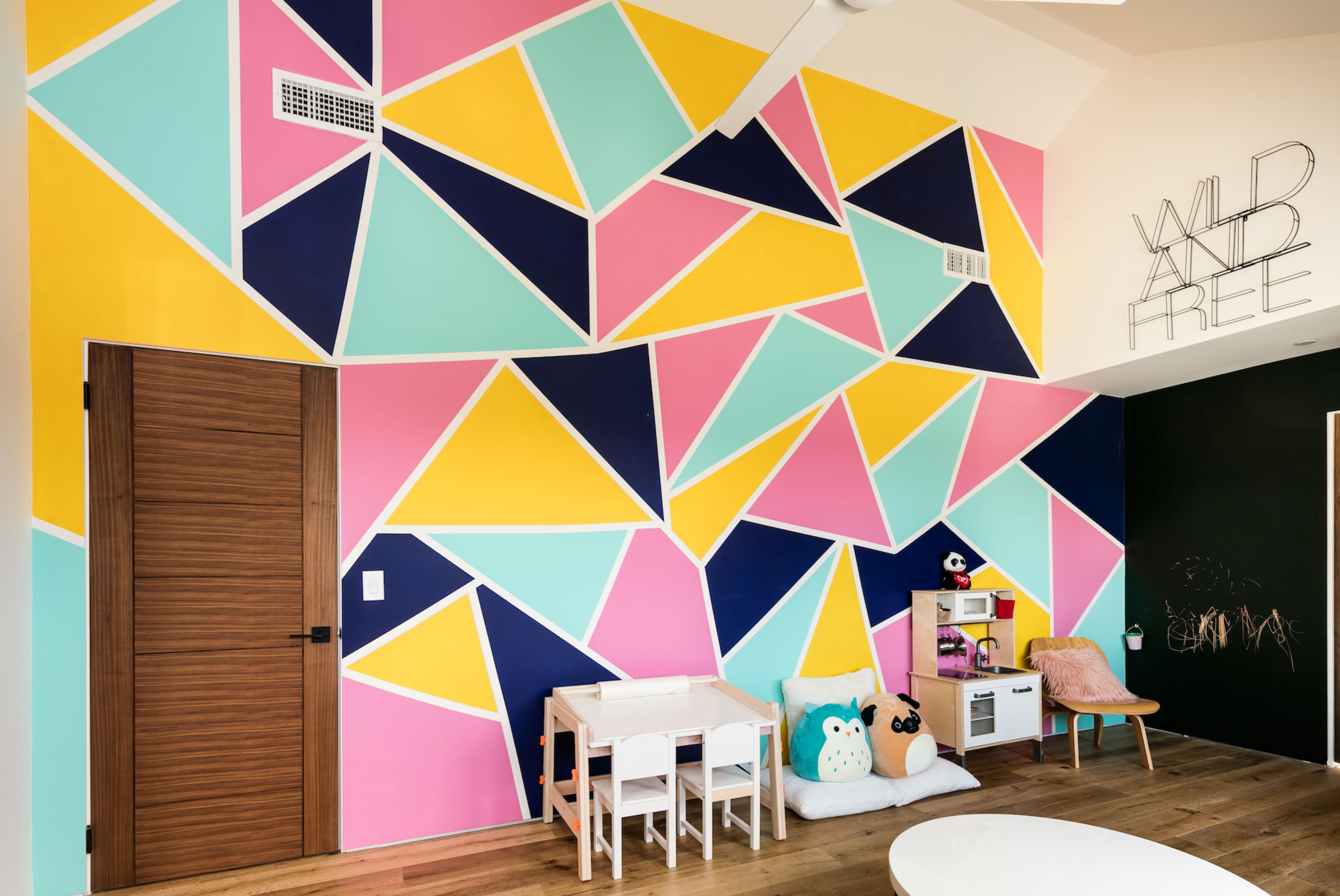 A children's room with a colorful geometric wall design featuring shades of pink, yellow, blue, and black, along with a small play area and toys.