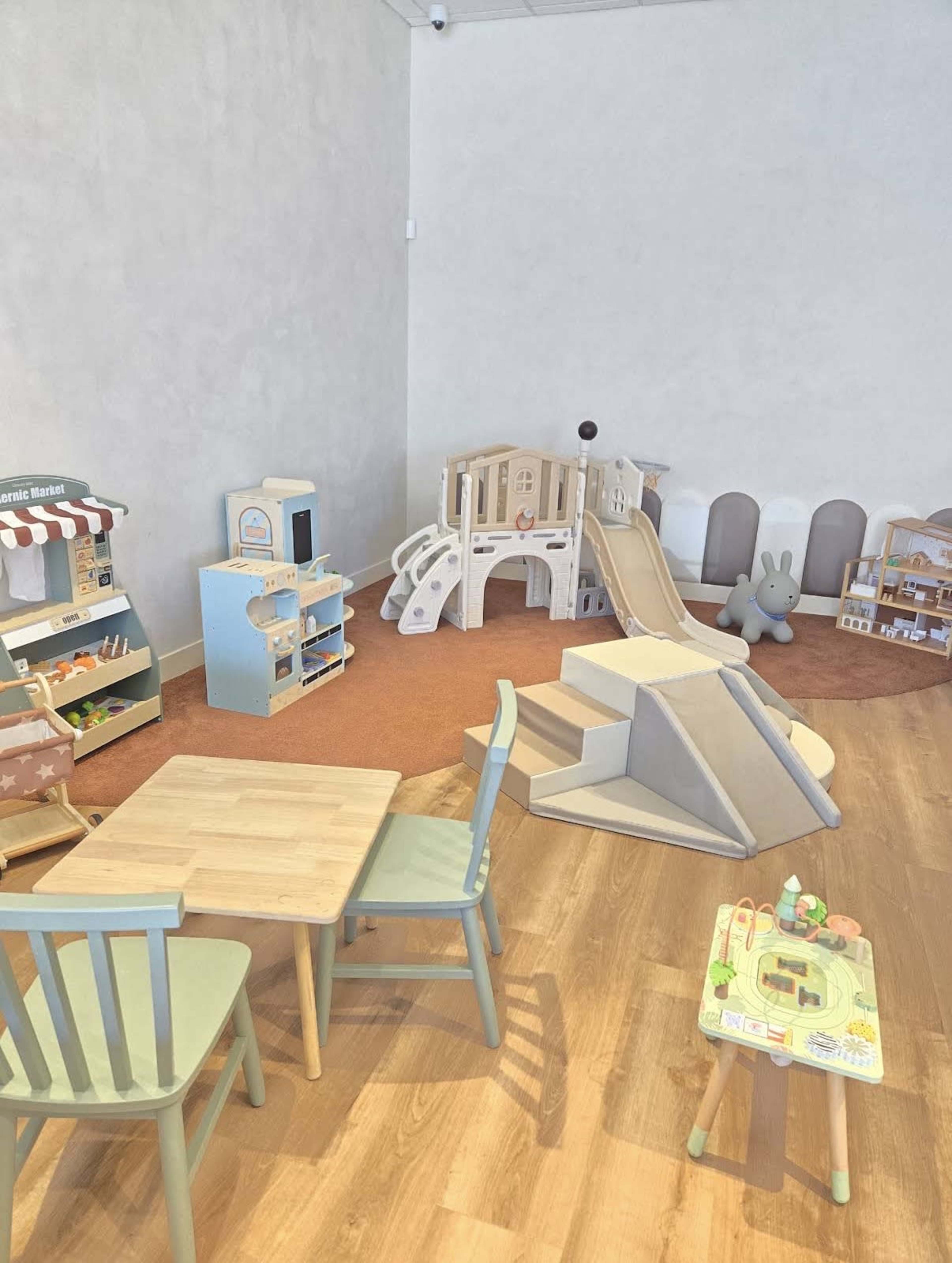 The image shows a children's playroom with various toy structures, including a slide, playhouses, and a small table with chairs.