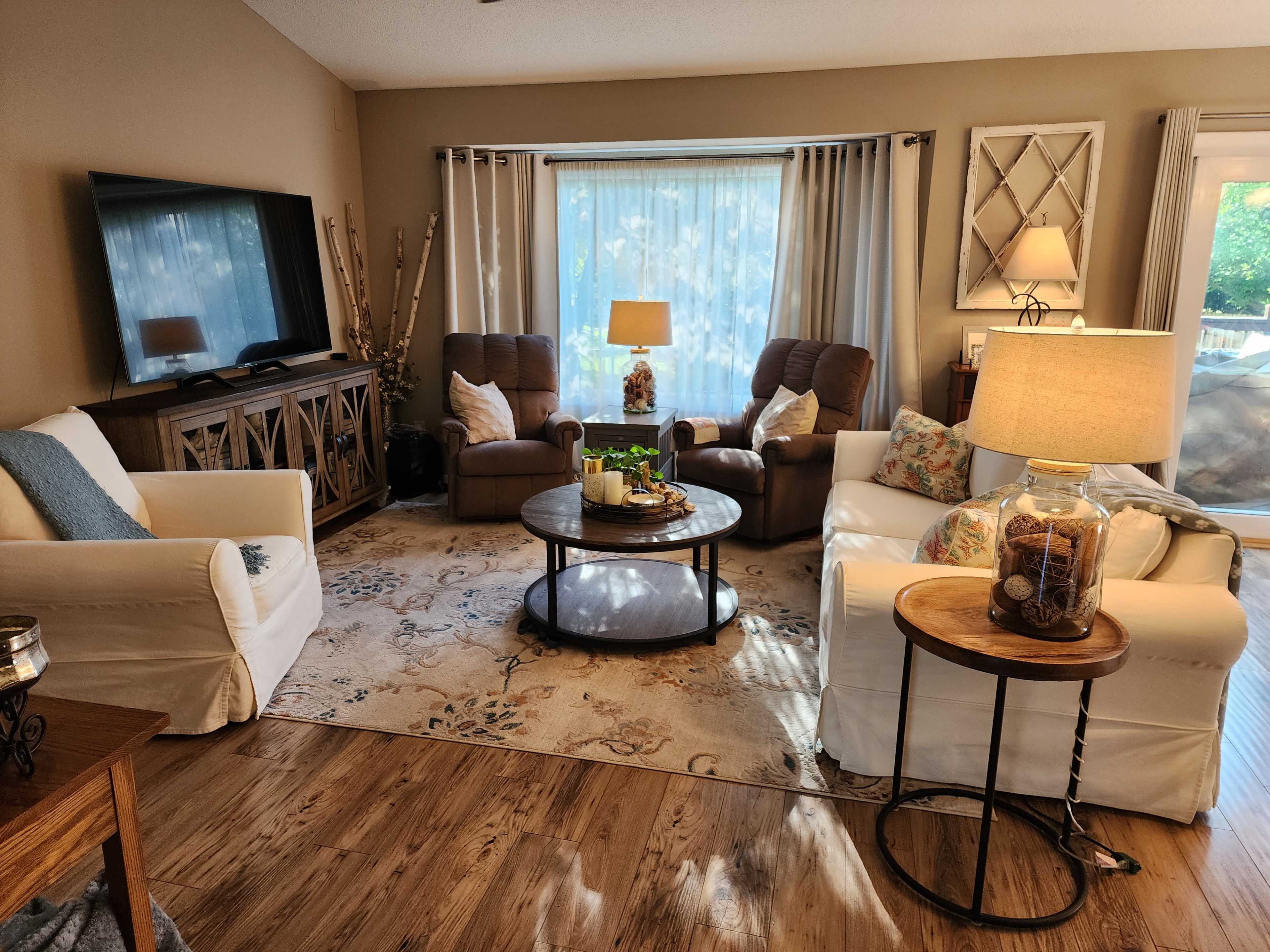 A cozy living room features two recliners, a coffee table with decorative items, and large windows letting in natural light.