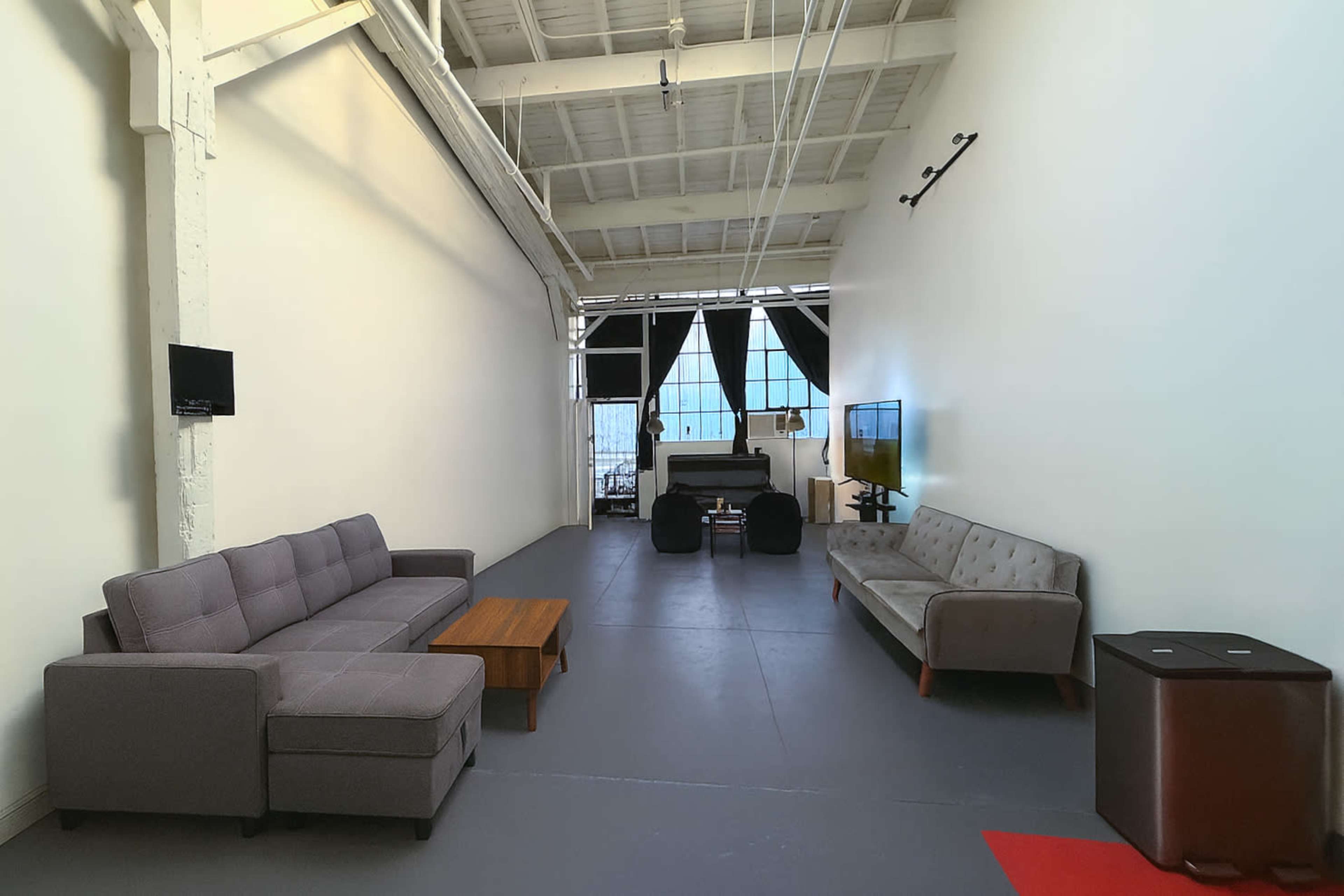 The image shows a spacious, minimalist interior with two sofas, a coffee table, a black chair, and a large window at the far end.