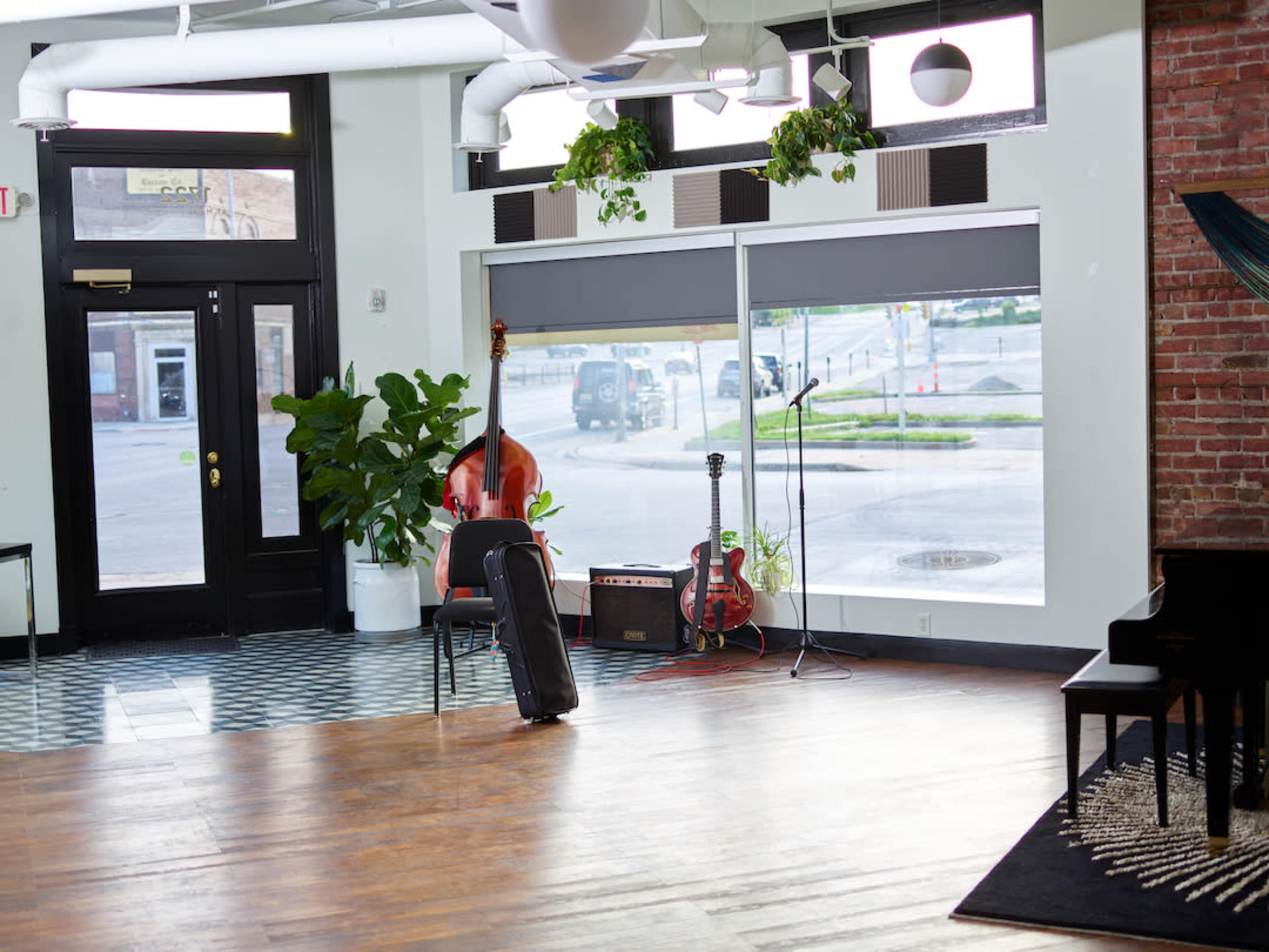 A spacious interior with wooden floors, a microphone stand, and musical instruments near a large window lined with plants.
