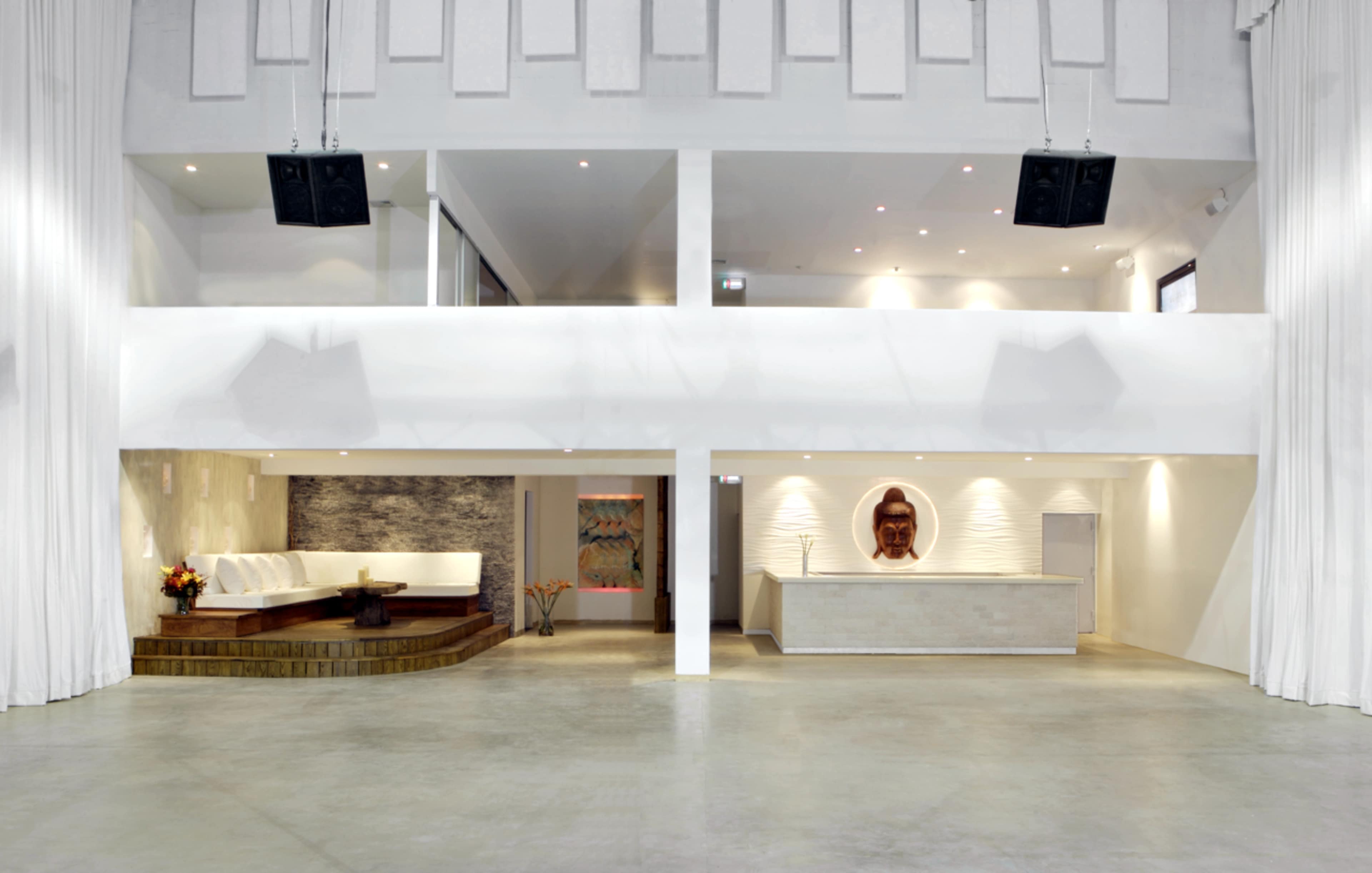 The image shows a spacious, modern venue featuring two levels, with a seating area on one side and a reception desk on the other.