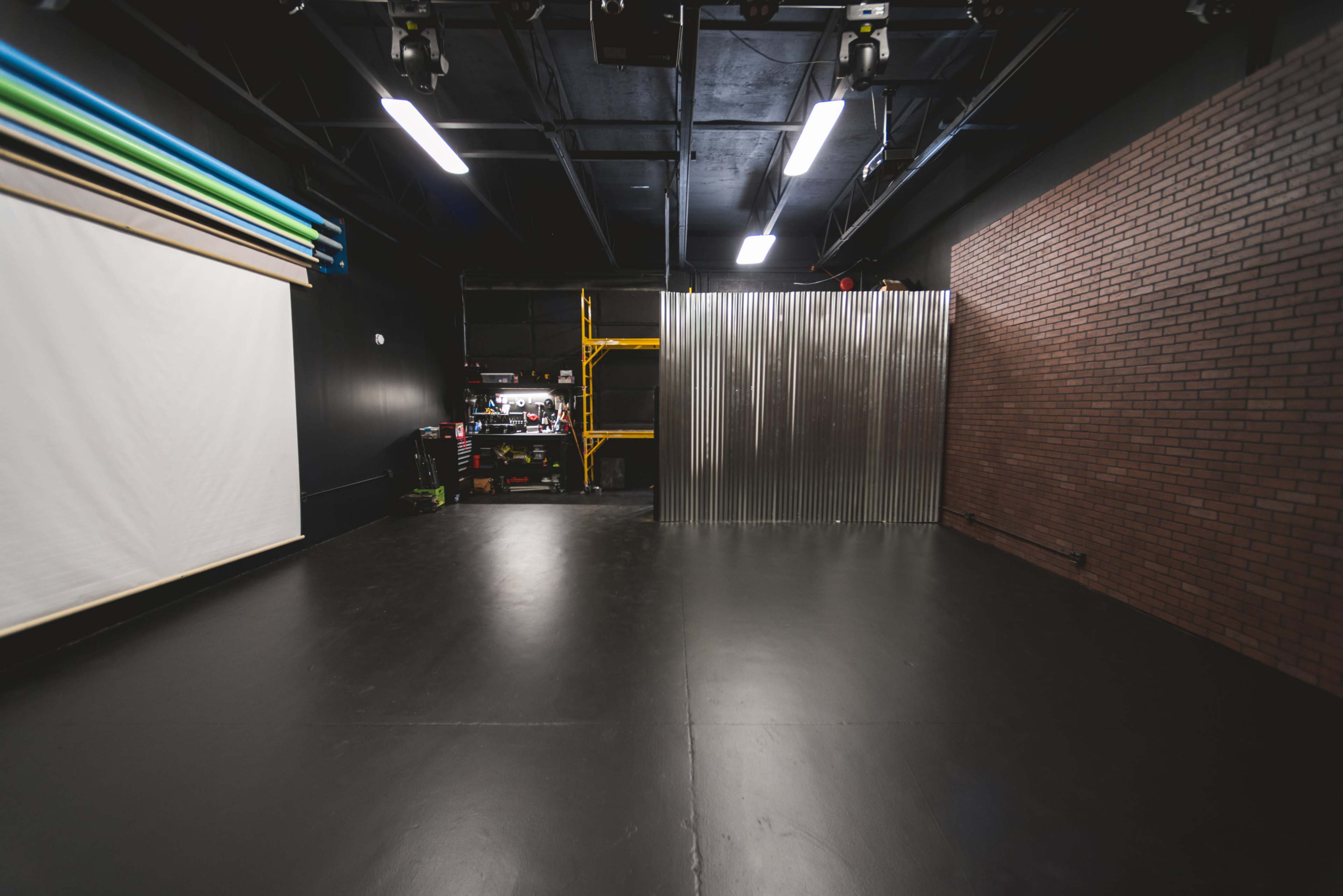A studio space with a black floor, a white backdrop, a corrugated metal wall, and a brick accent wall.