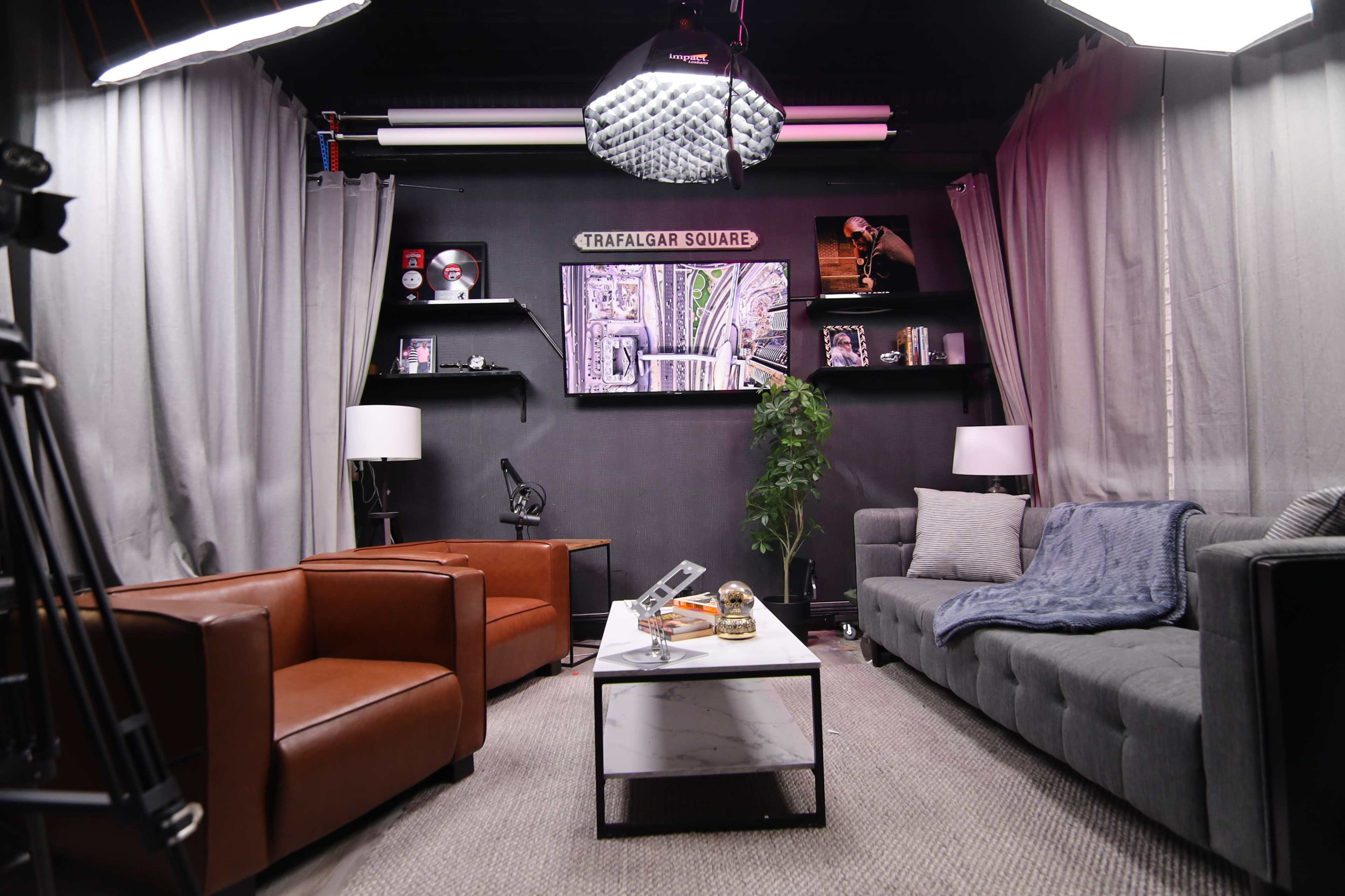 A modern living room setup with two leather sofas, a coffee table, decorative art on the walls, and studio lighting.
