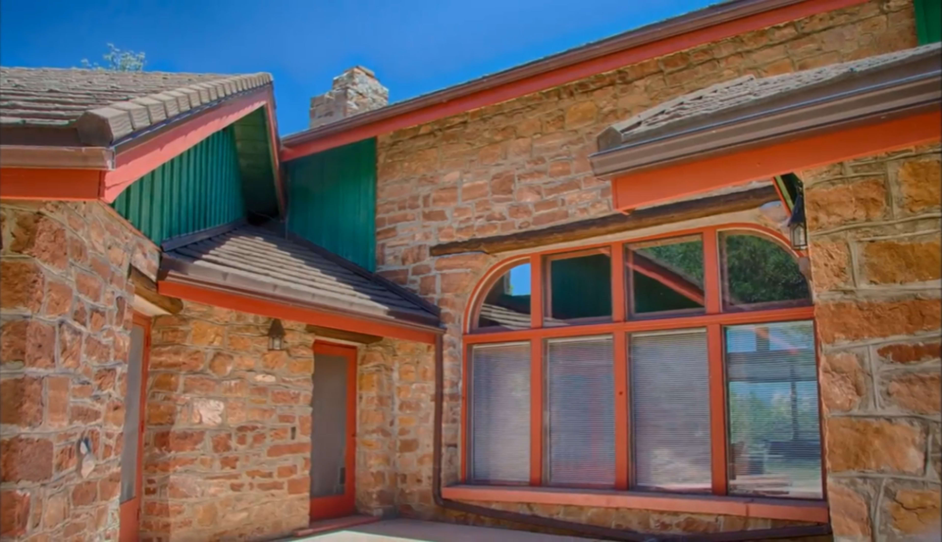 A stone house featuring a distinct angular design, large windows, and a combination of green and orange trim.