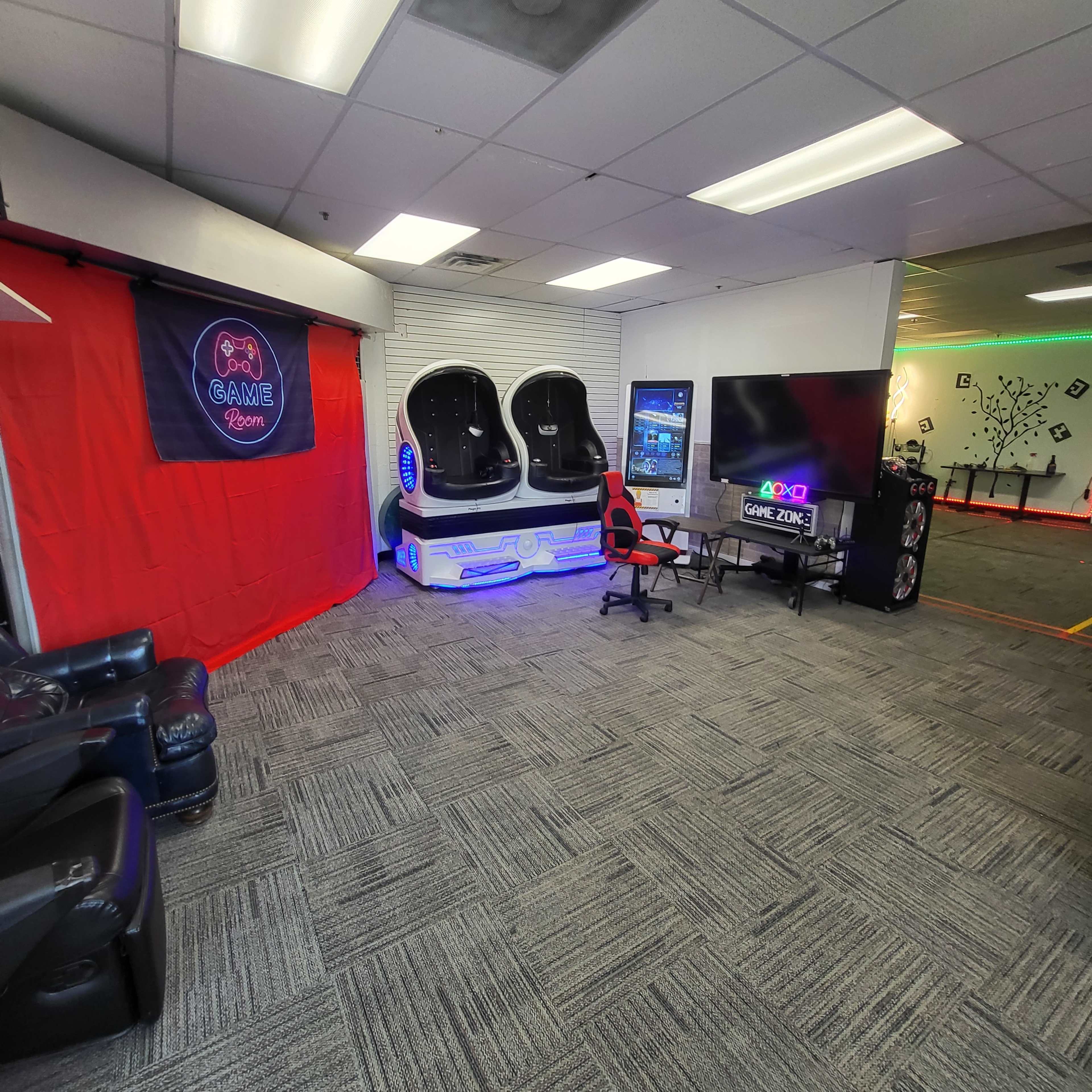 The image shows a game room featuring gaming chairs, a large television, and a red backdrop with a "Game Room" sign.