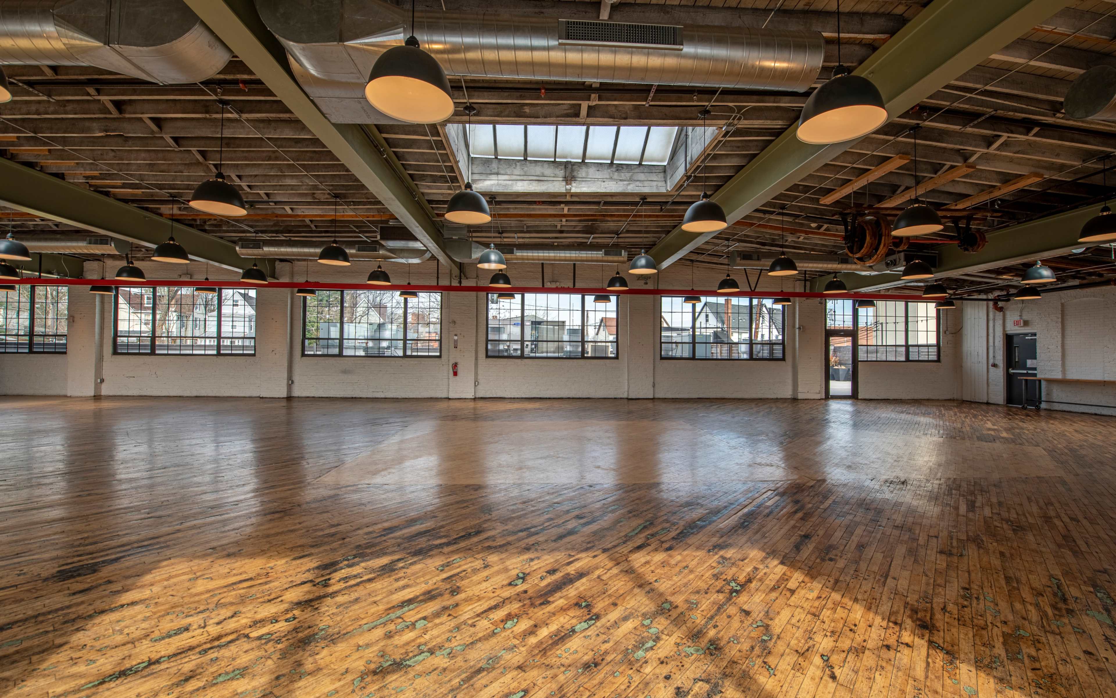 A spacious, empty industrial-style room with large windows and wooden floors.