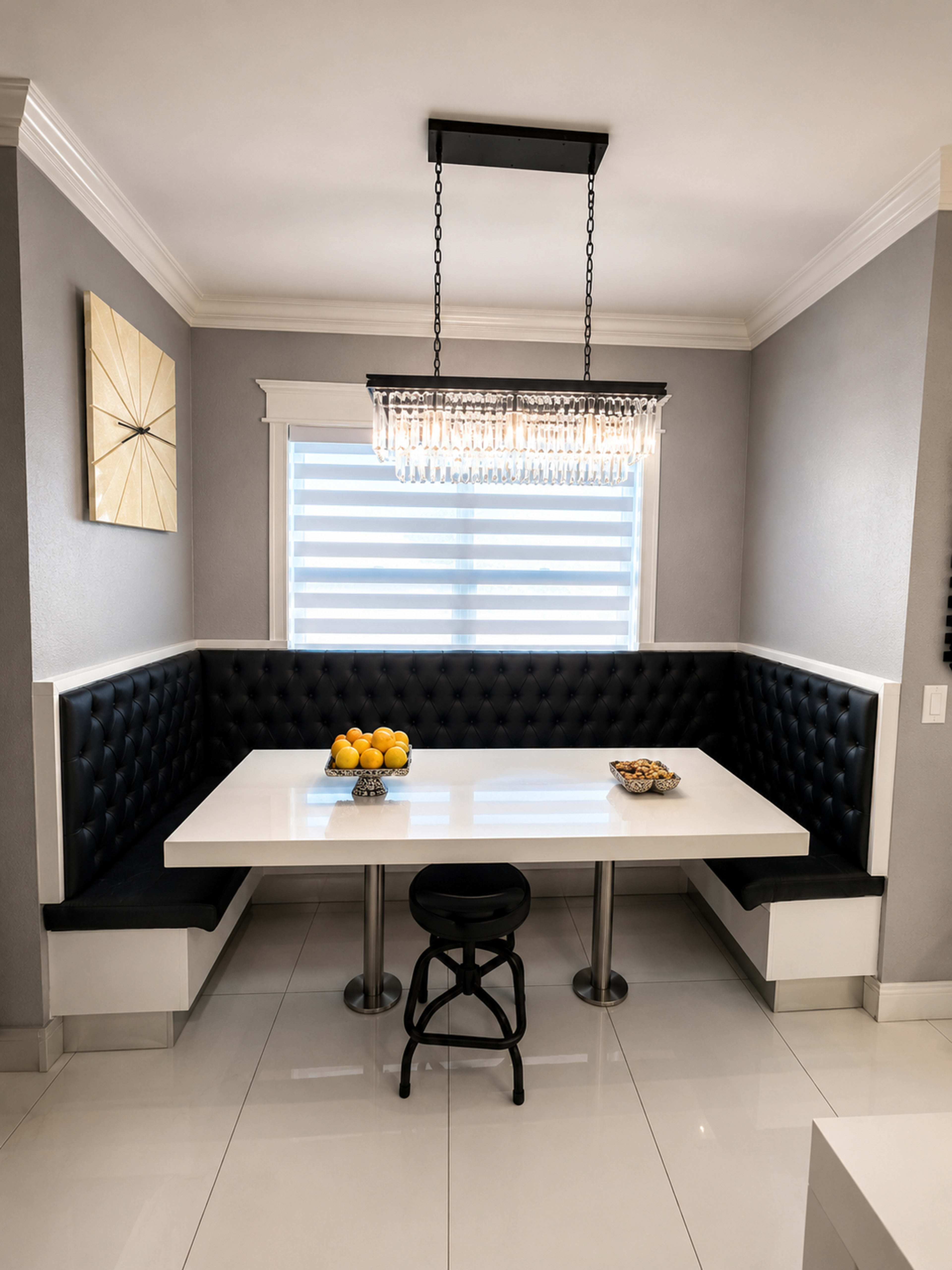 A modern dining nook features a white table, black tufted seating, and a chandelier above, with a bowl of lemons as a centerpiece.