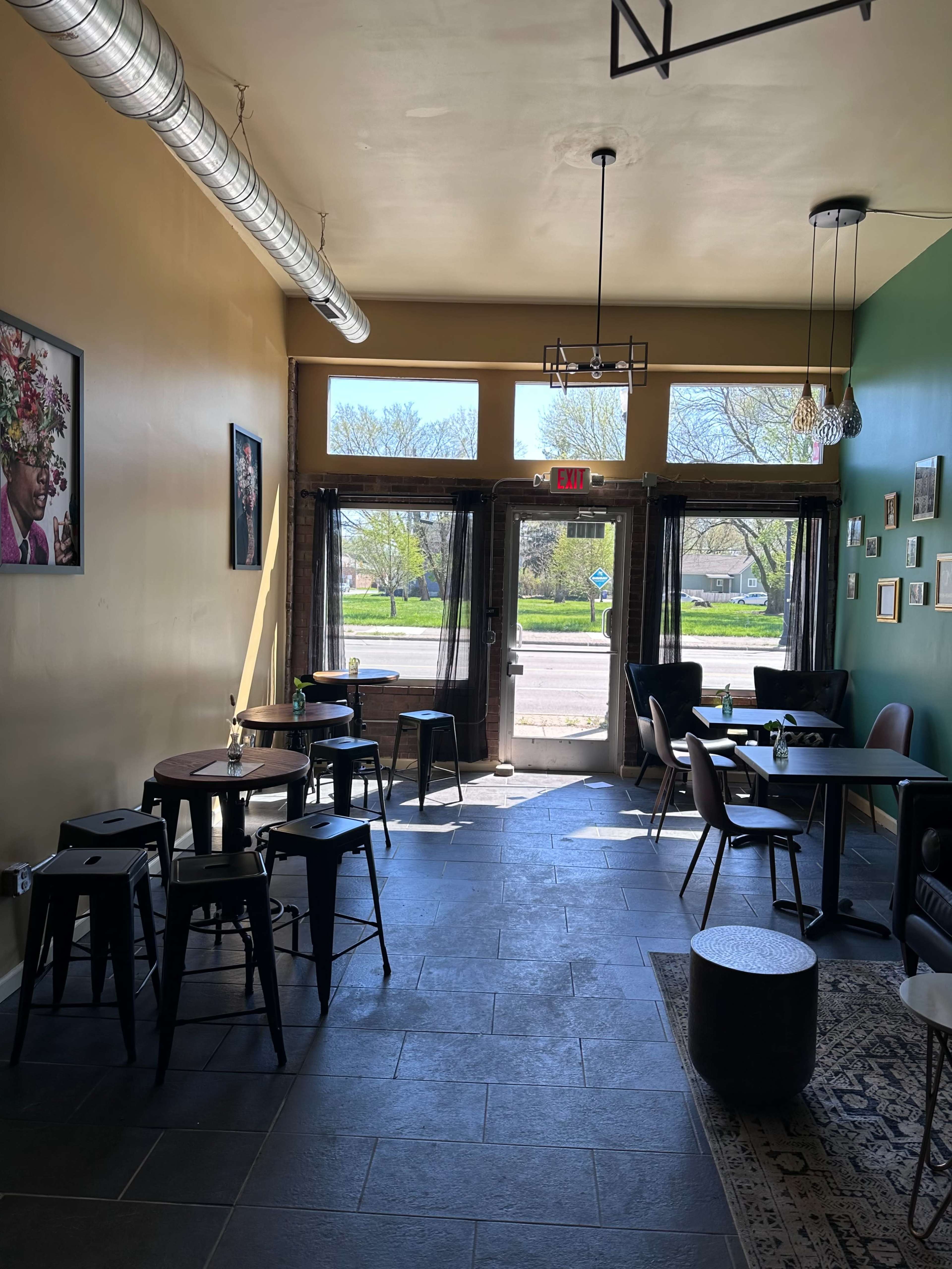 A cafe interior with tables and chairs arranged along the walls and large windows allowing natural light to enter.