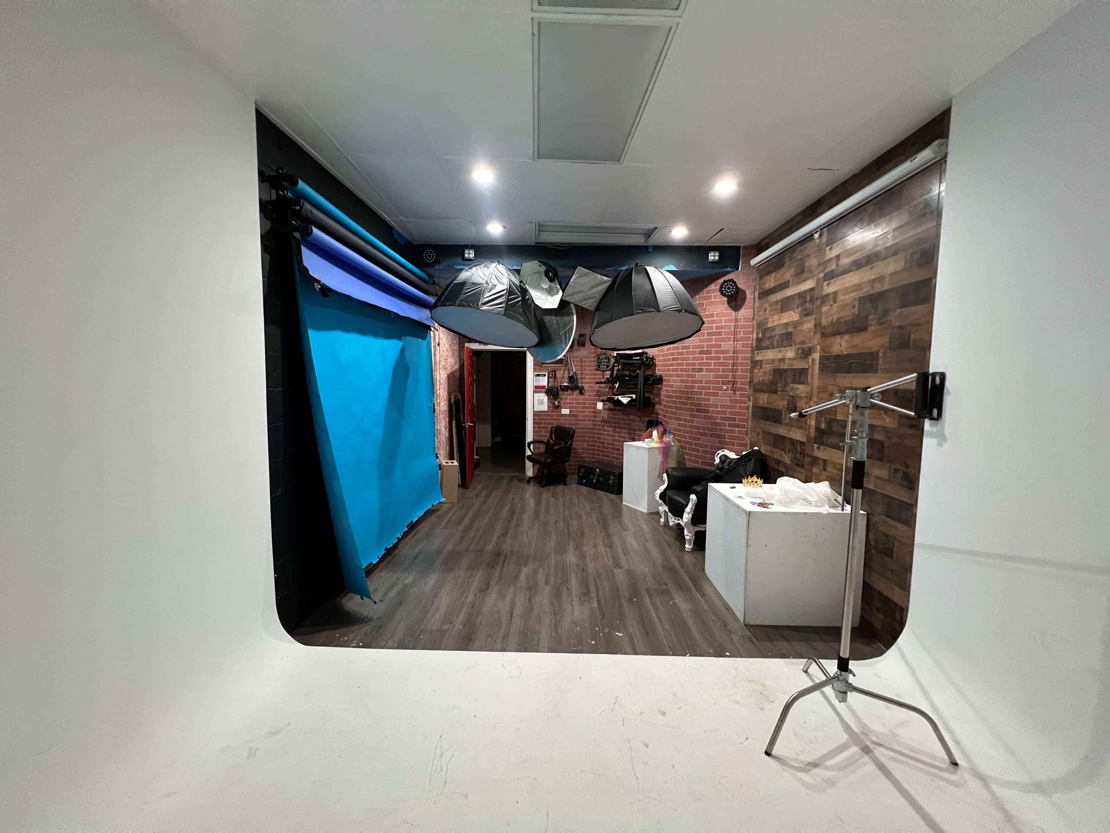 A studio space featuring a blue backdrop, wooden walls, and lighting equipment suspended overhead.
