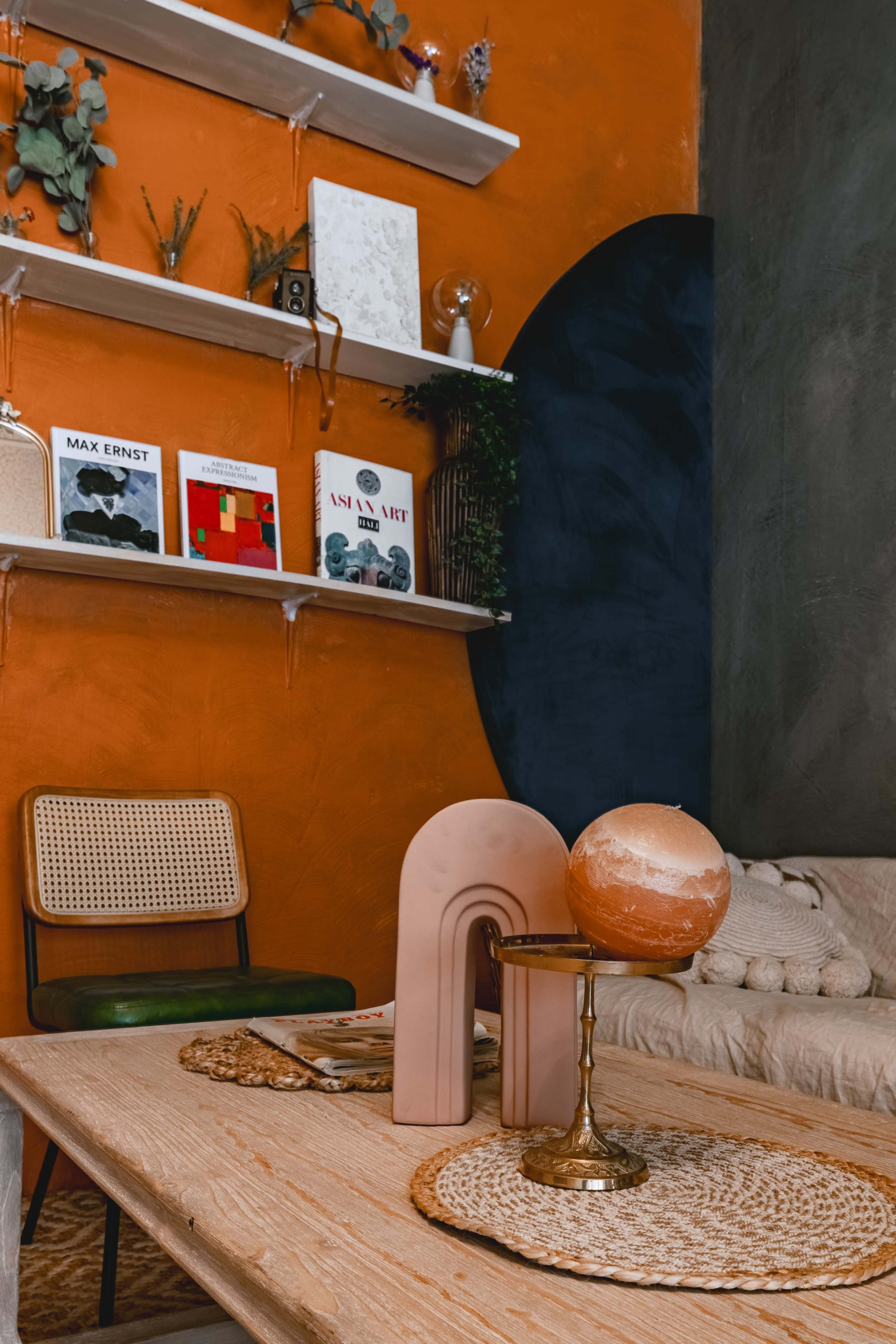 A cozy interior with an orange wall, shelves displaying books and decorative items, and a wooden table featuring a decorative arch and a globe.