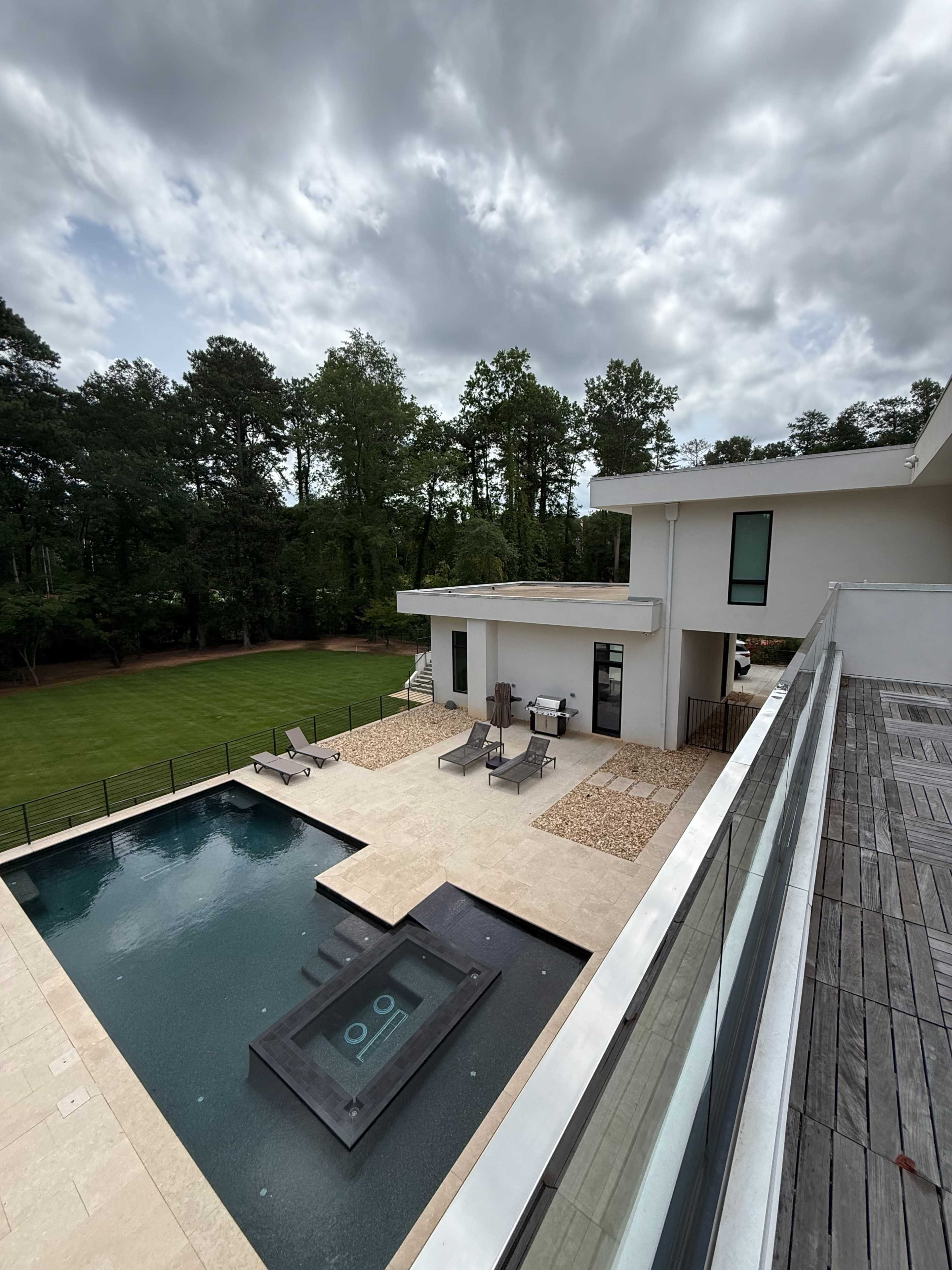 The image shows a modern house with a swimming pool and a landscaped yard under a cloudy sky.