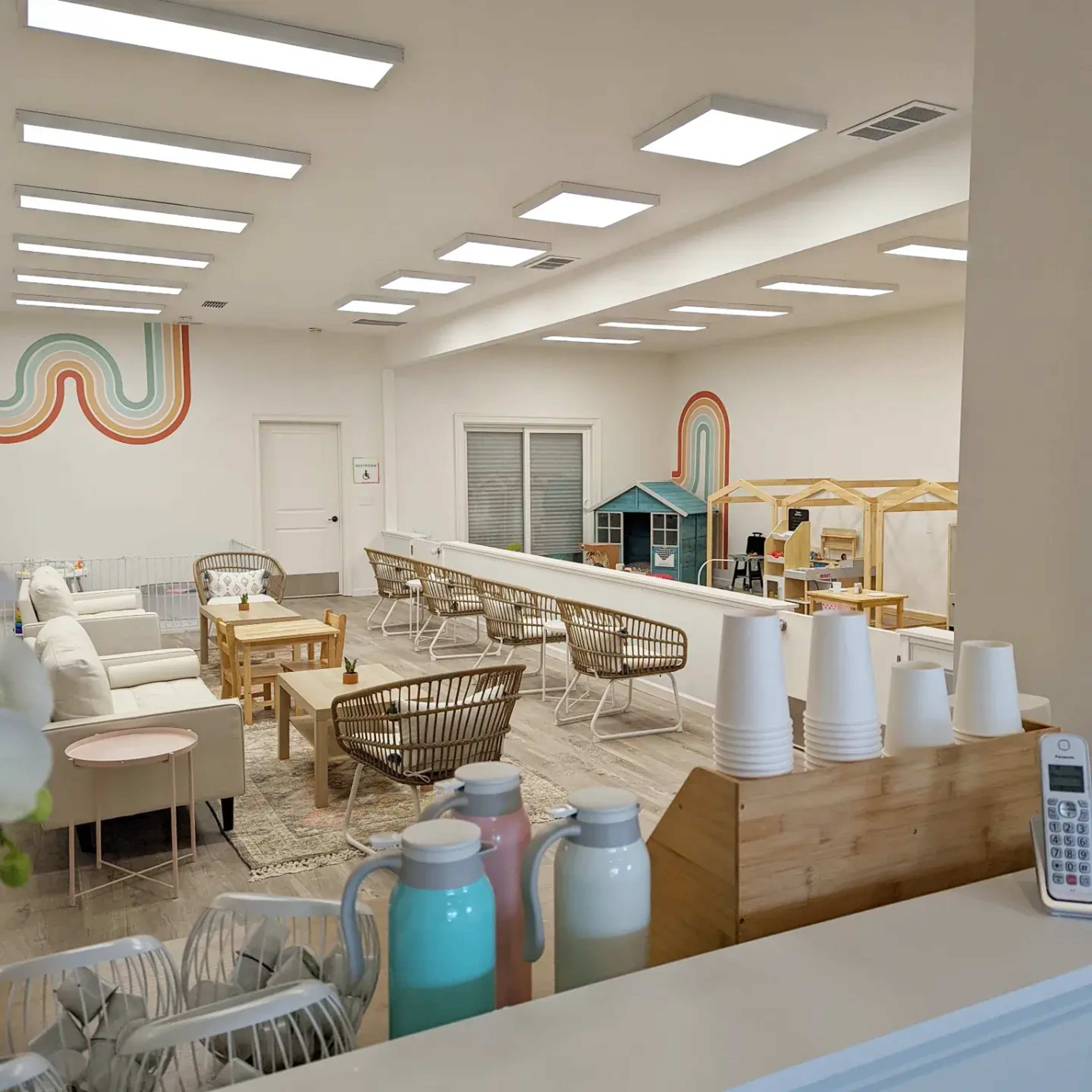 A bright, spacious room with various seating areas, colorful wall decorations, and play structures for children.