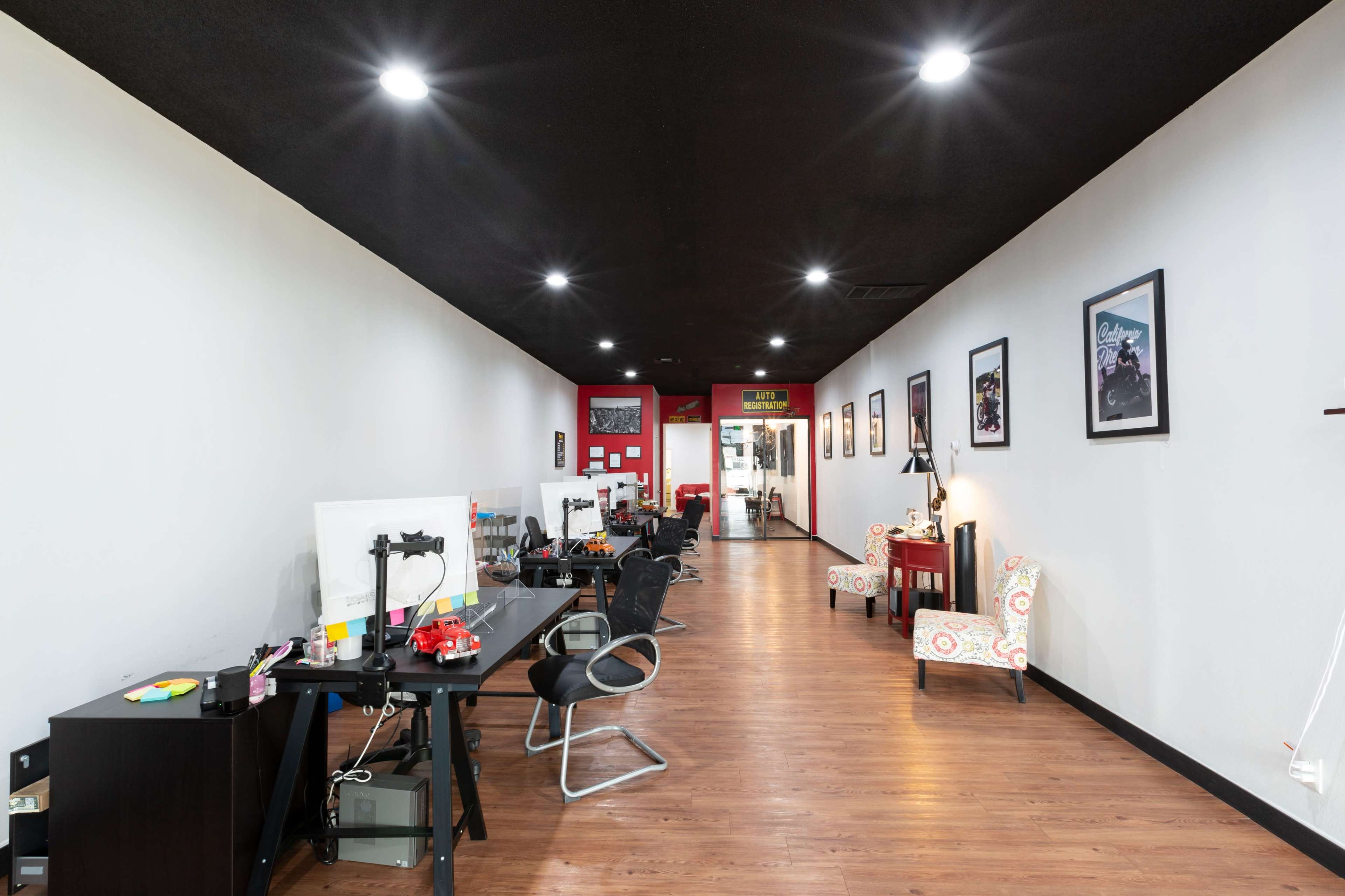 A long, narrow office space with dark ceilings, brightly lit areas, several workstations, and decorative seating along the walls.