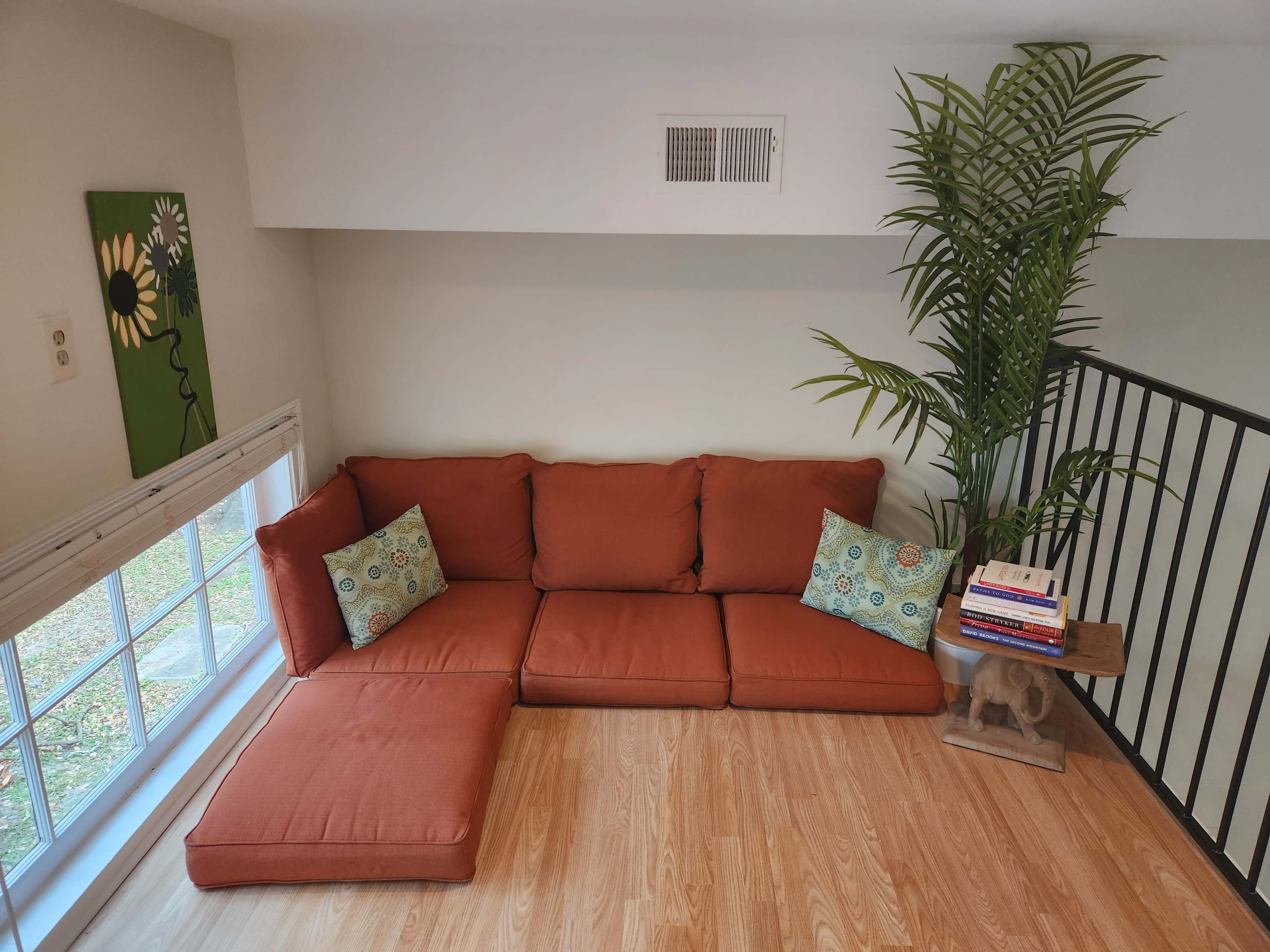 A sectional couch in an indoor space is positioned next to a large window, with decorative pillows and a side table holding books and a decorative object.