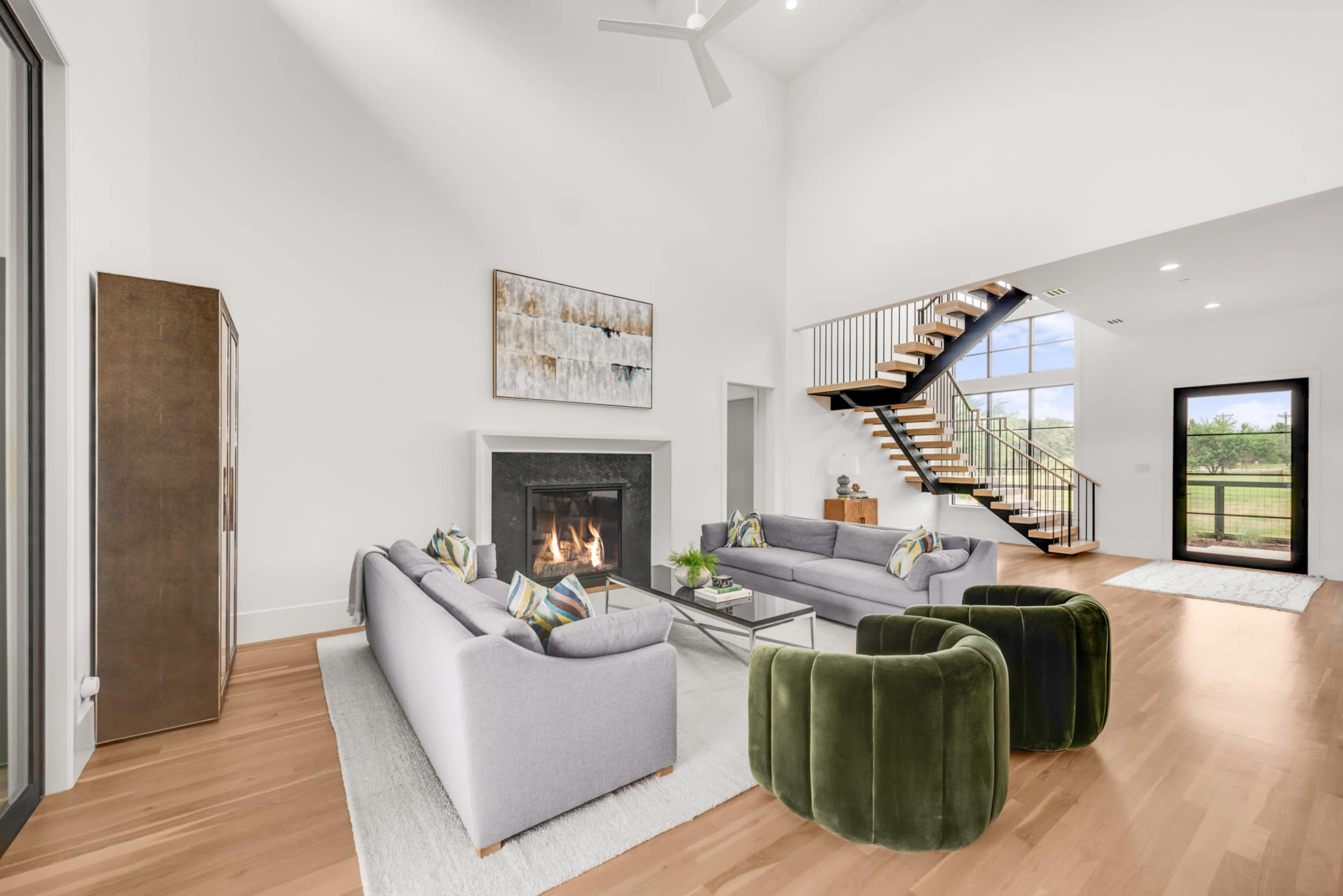 The spacious living room features a large fireplace, modern seating arrangements, and a staircase leading to an upper level.
