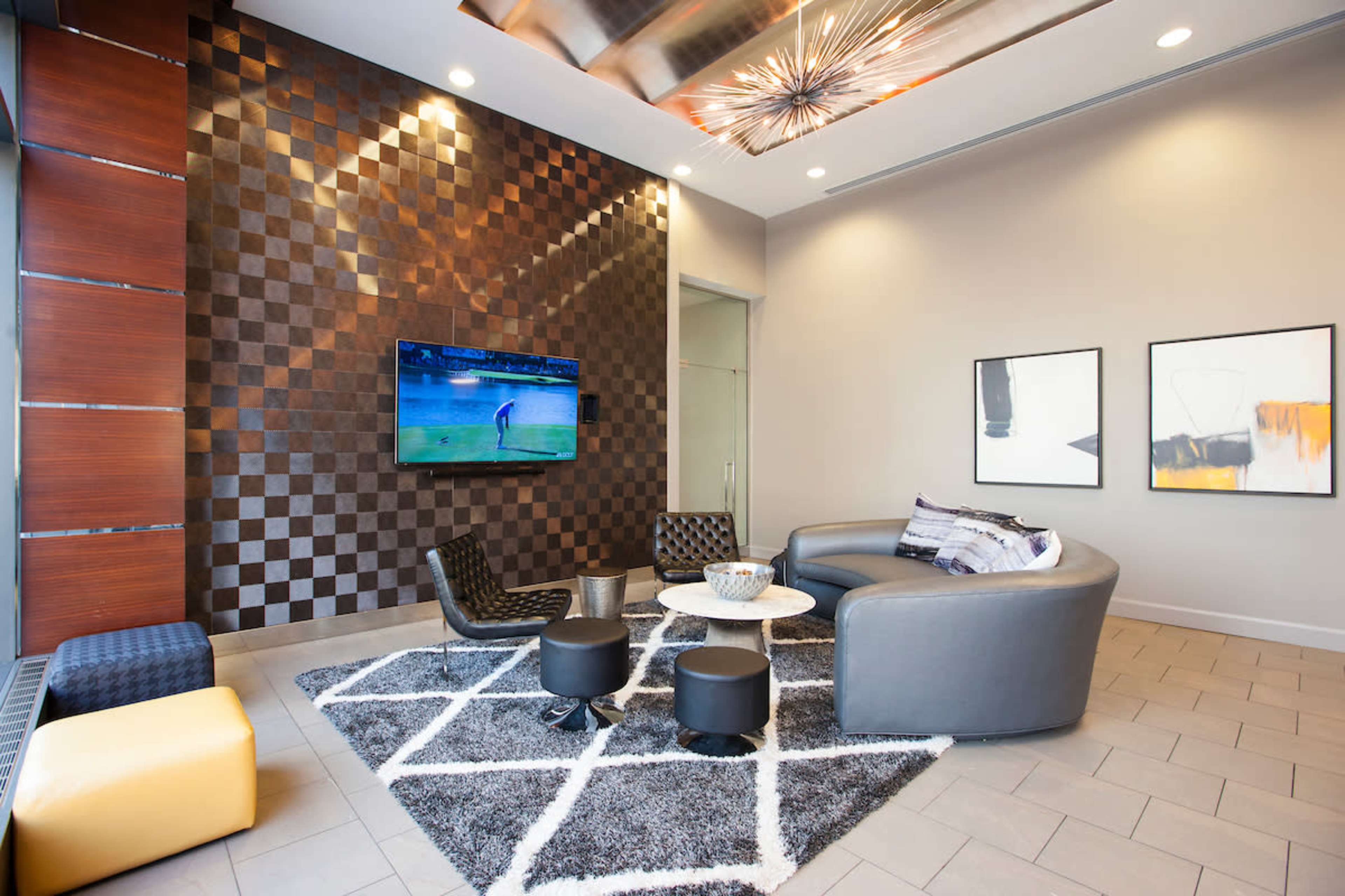 A modern lounge area with a patterned wall, a large television, two armchairs, a circular coffee table, and abstract artwork hanging on the walls.