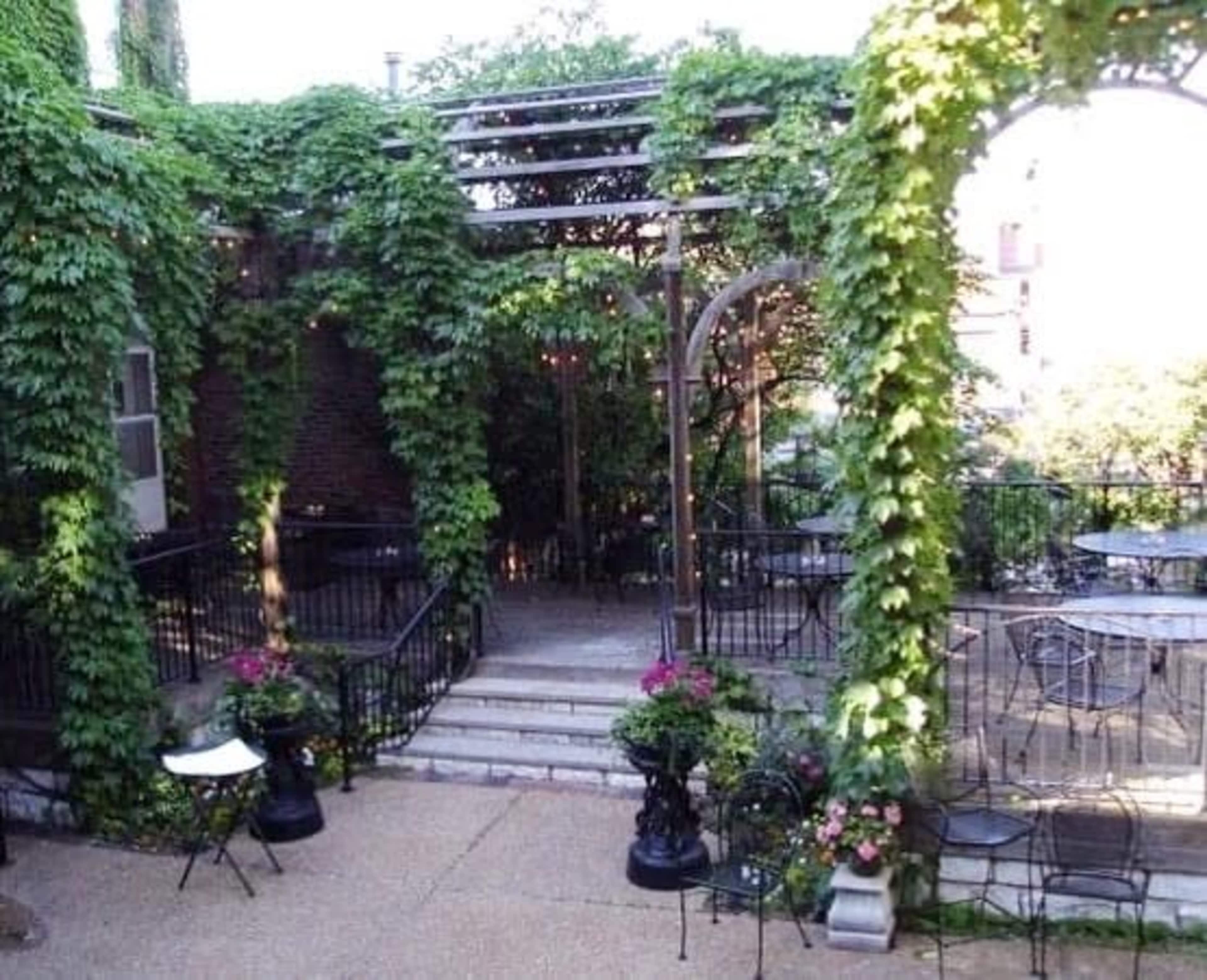 A courtyard is surrounded by greenery and features wrought iron furniture, stone steps, and decorative planters.