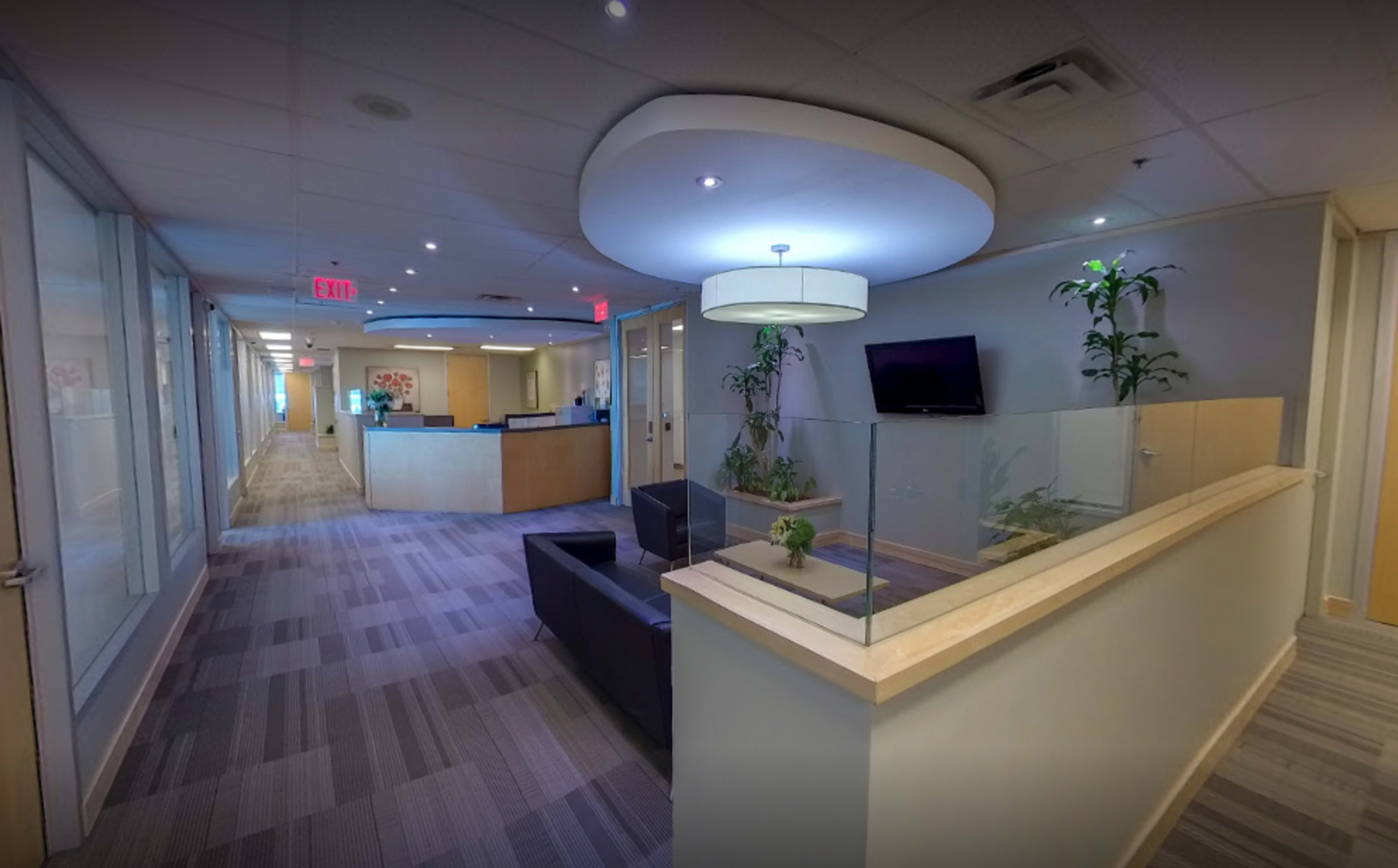 A modern office lobby with a reception area, seating, and plants, featuring large windows and a neutral color palette.
