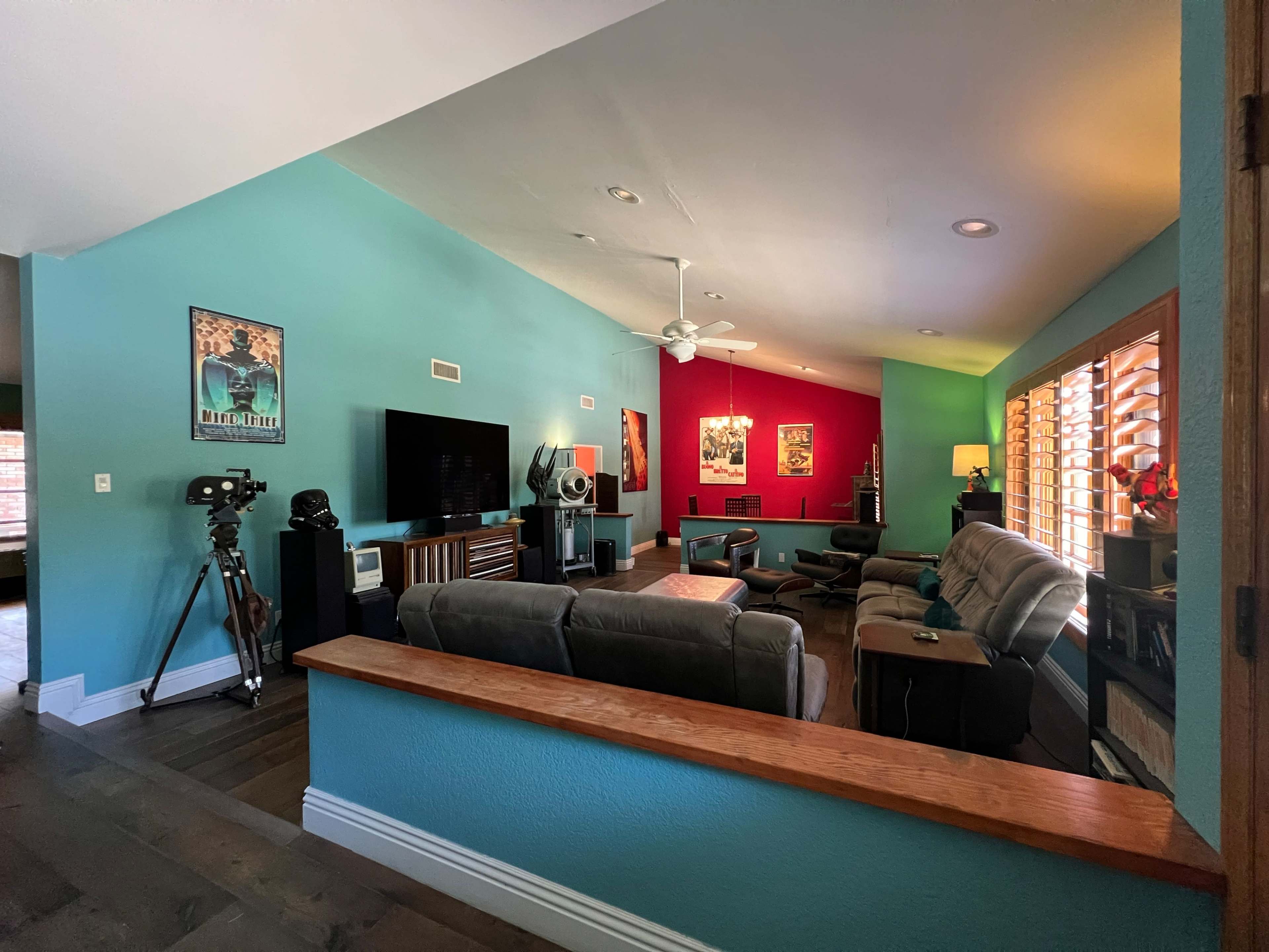A living room with colorful walls, a television, seating arrangements, and a mix of decor, including a camera tripod and framed art.