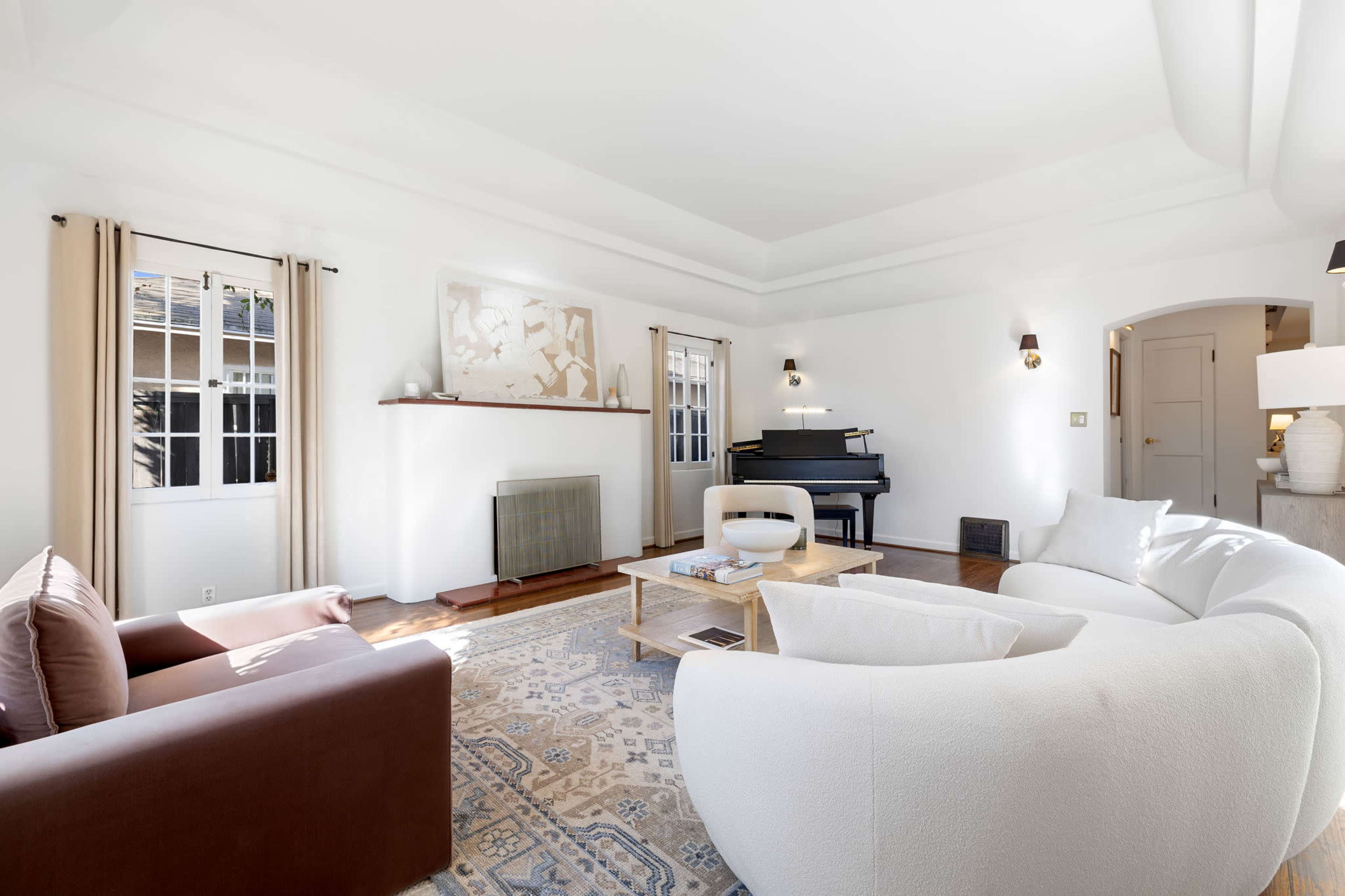 The living room features a piano, a circular white sofa, a brown armchair, and a central coffee table on an area rug.