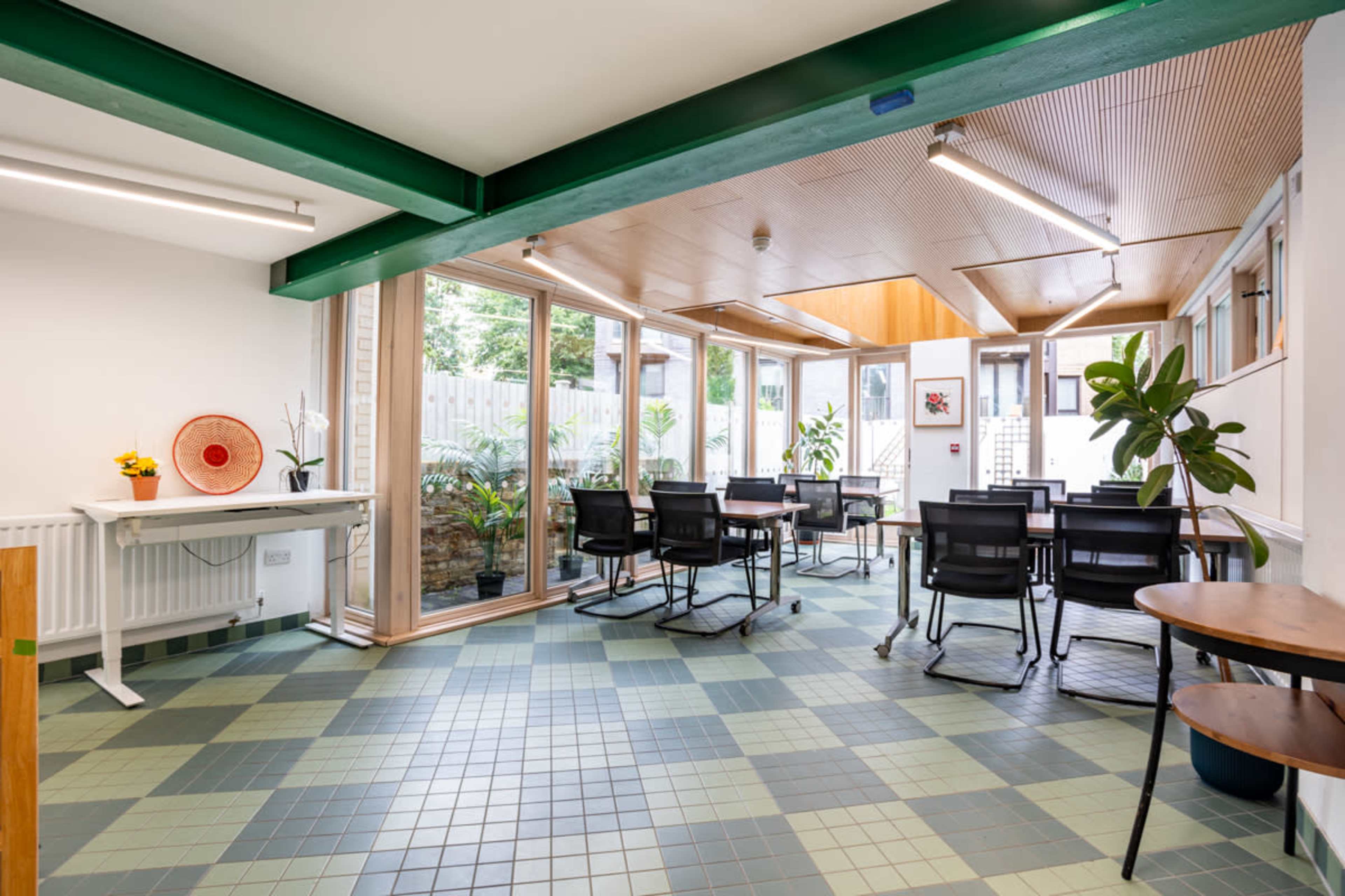 A bright, modern meeting room with green and blue tiled flooring, surrounded by large windows and office furniture.