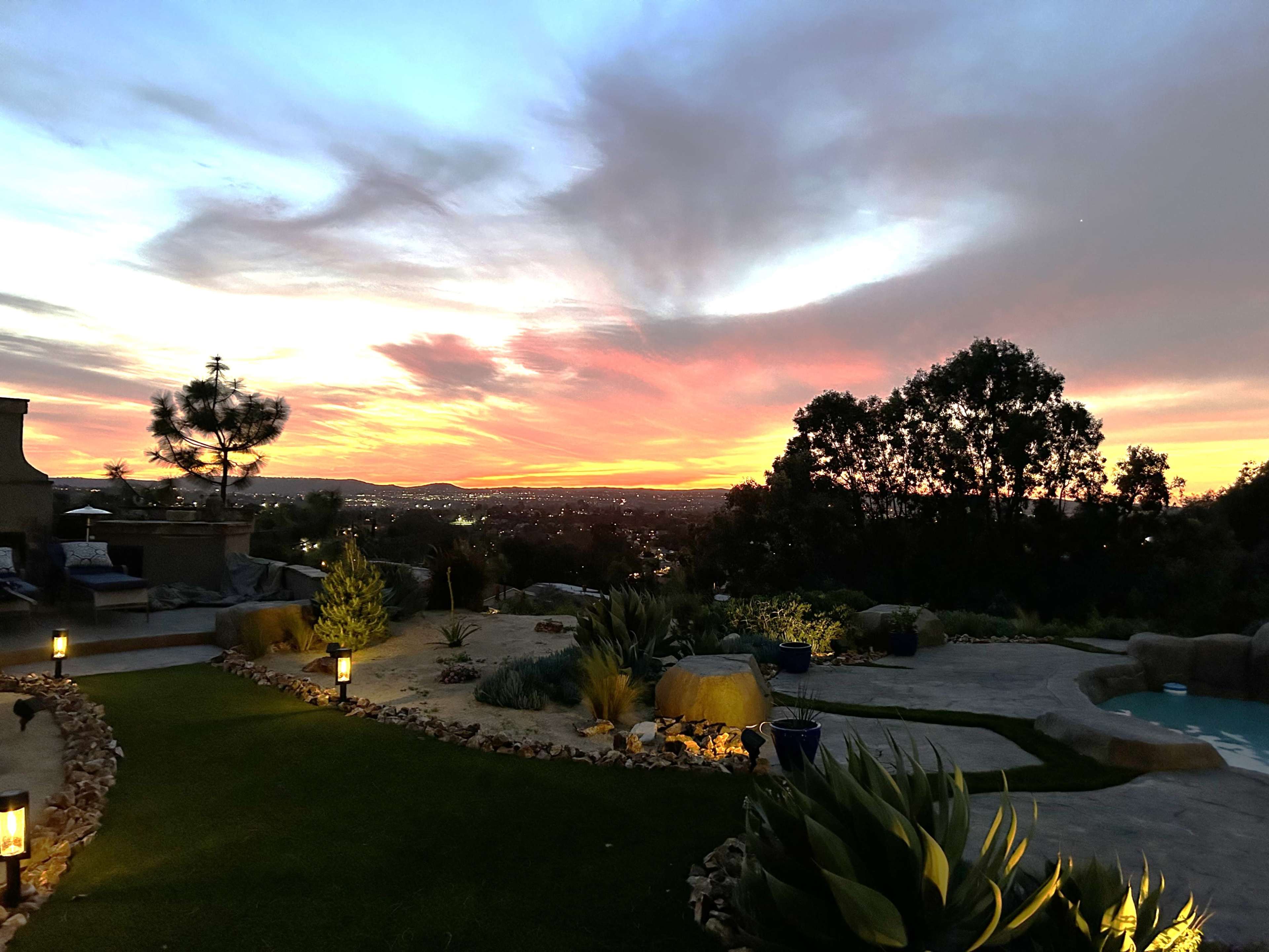 A landscaped outdoor area with plants and light fixtures illuminated against a vibrant sunset sky.