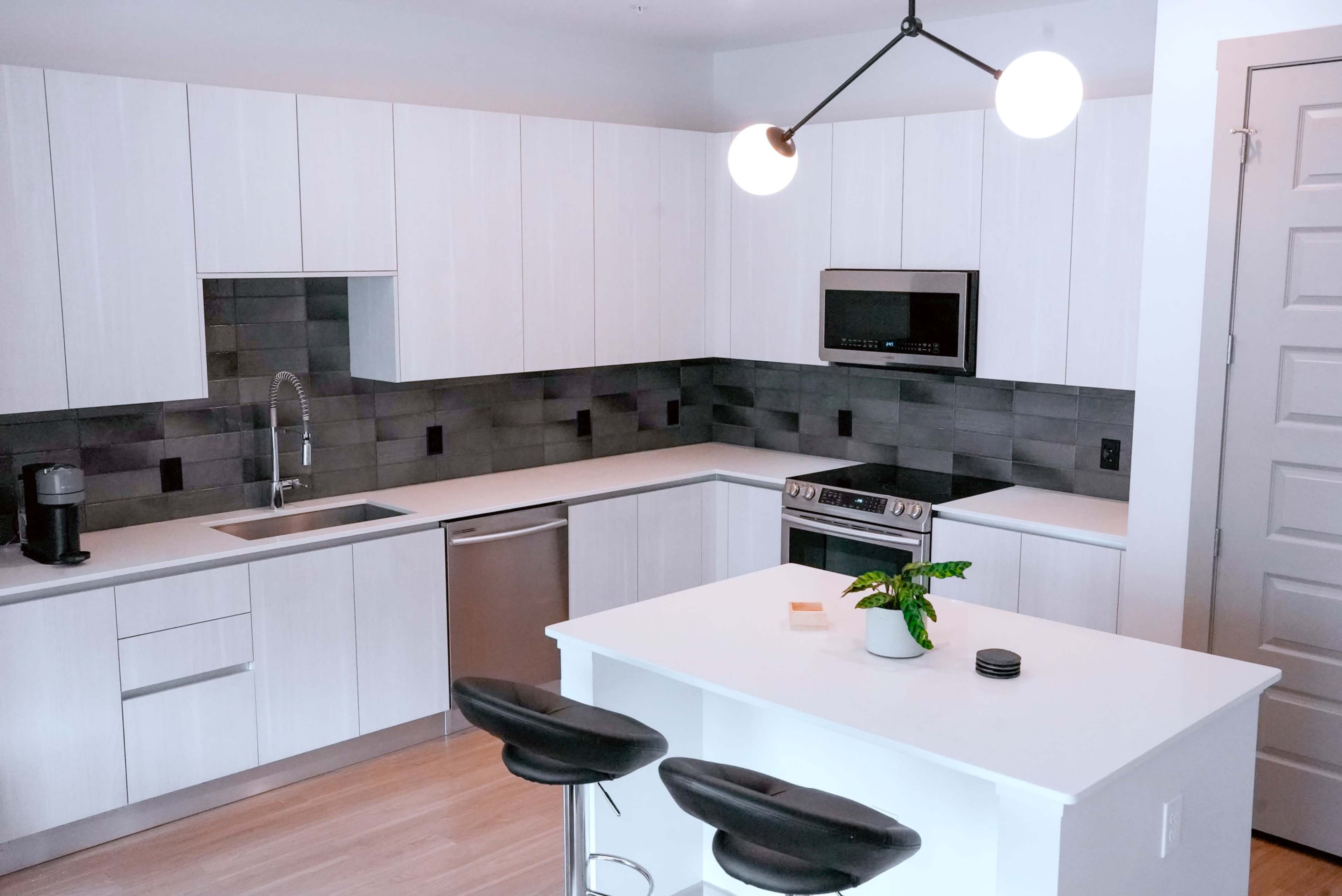 A modern kitchen with white cabinetry, stainless steel appliances, and a central island with black bar stools.