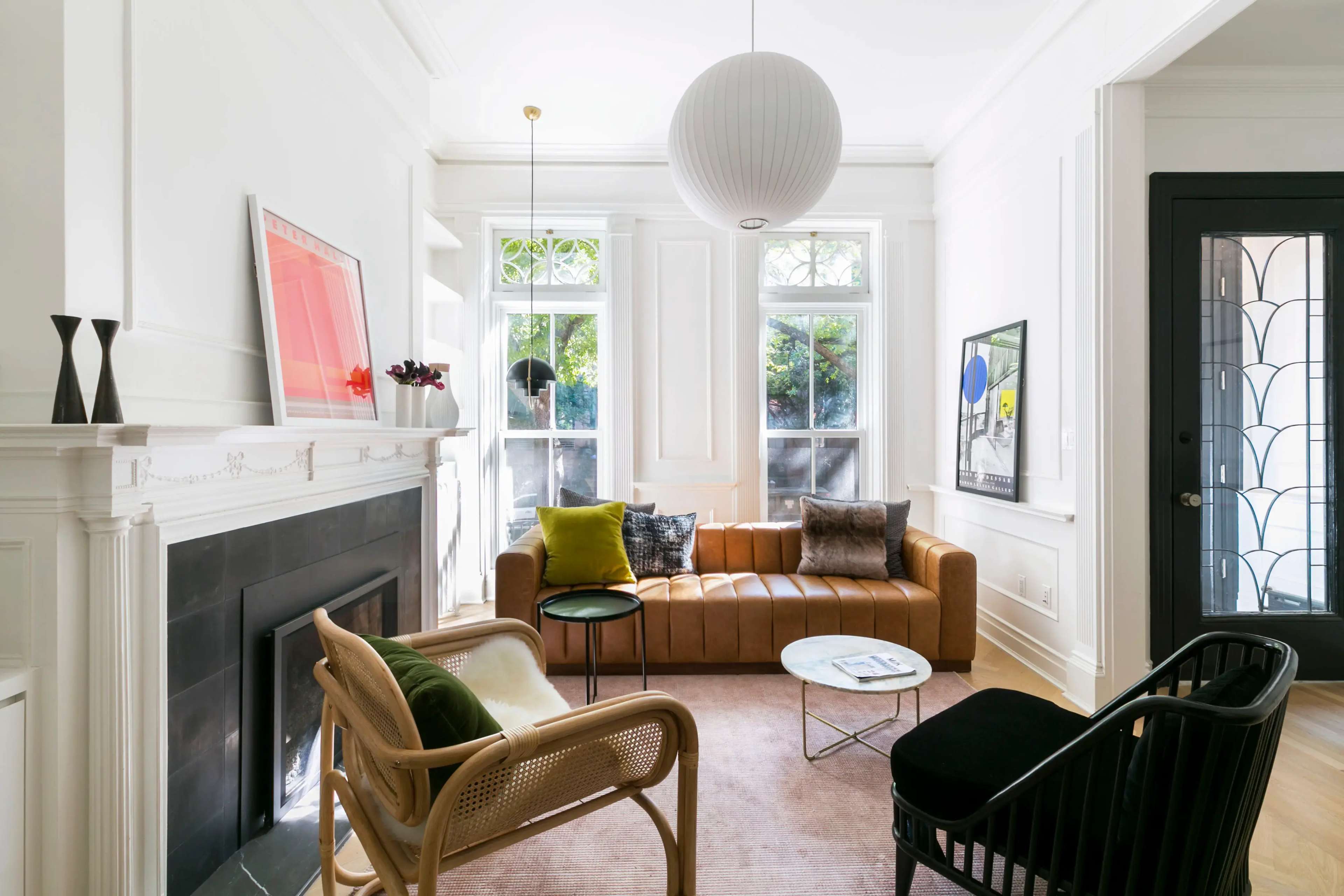 A modern living room features a brown leather sofa, a black accent chair, a round coffee table, and large windows with natural light.