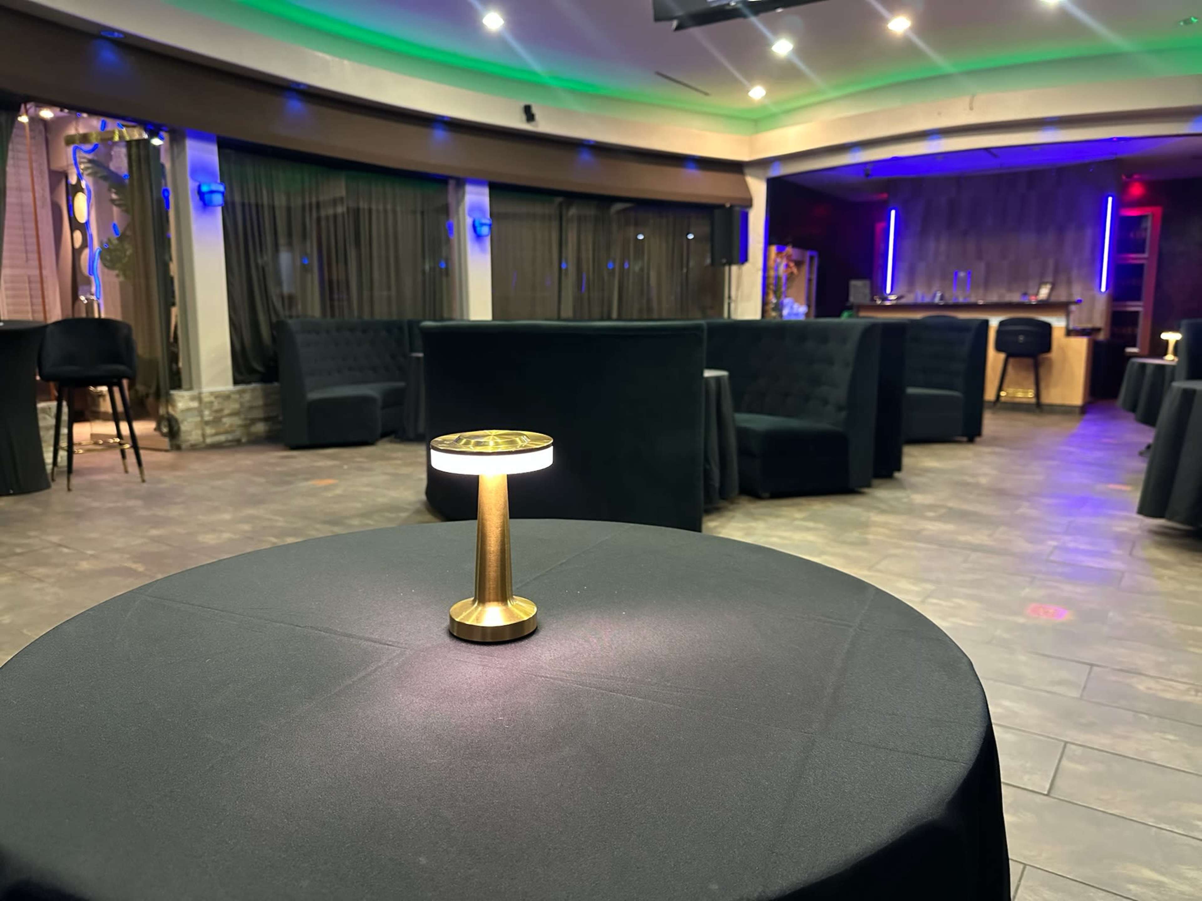 A well-lit table with a small lamp stands in a modern lounge area featuring dark furnishings and illuminated accents.