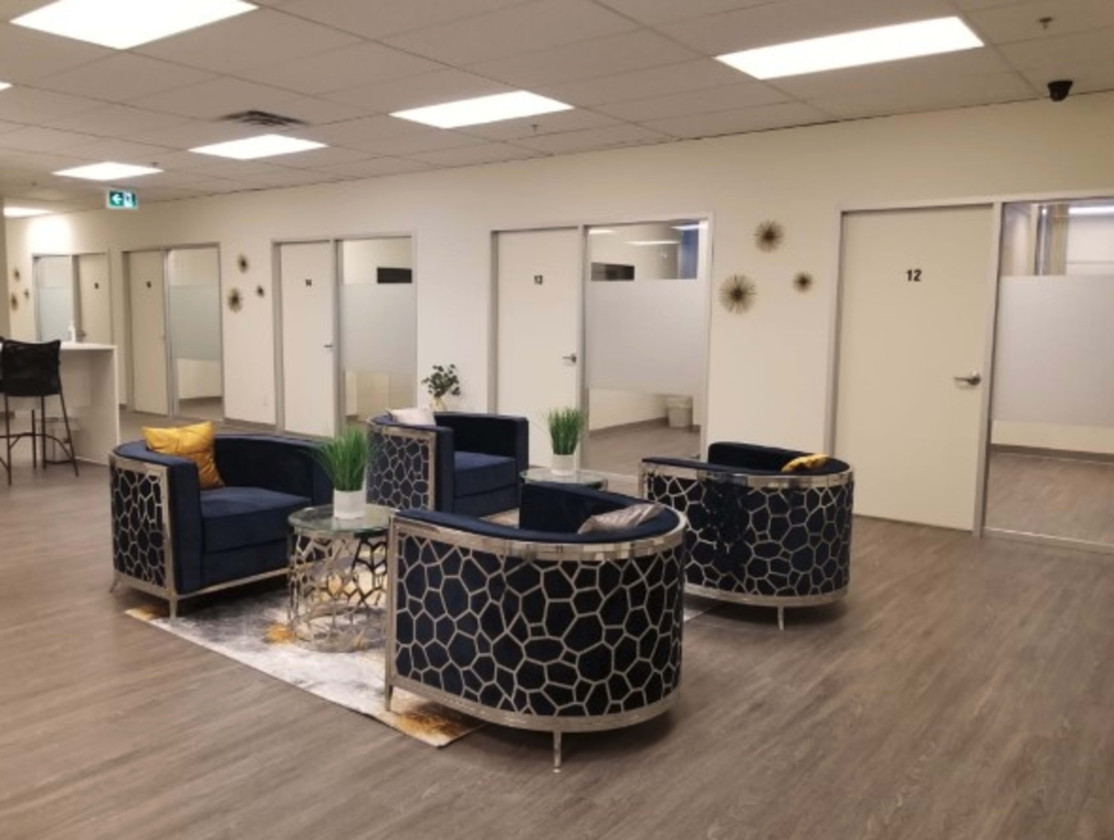 A modern waiting area featuring two circular seating arrangements with blue chairs, a glass table, and several closed office doors in the background.