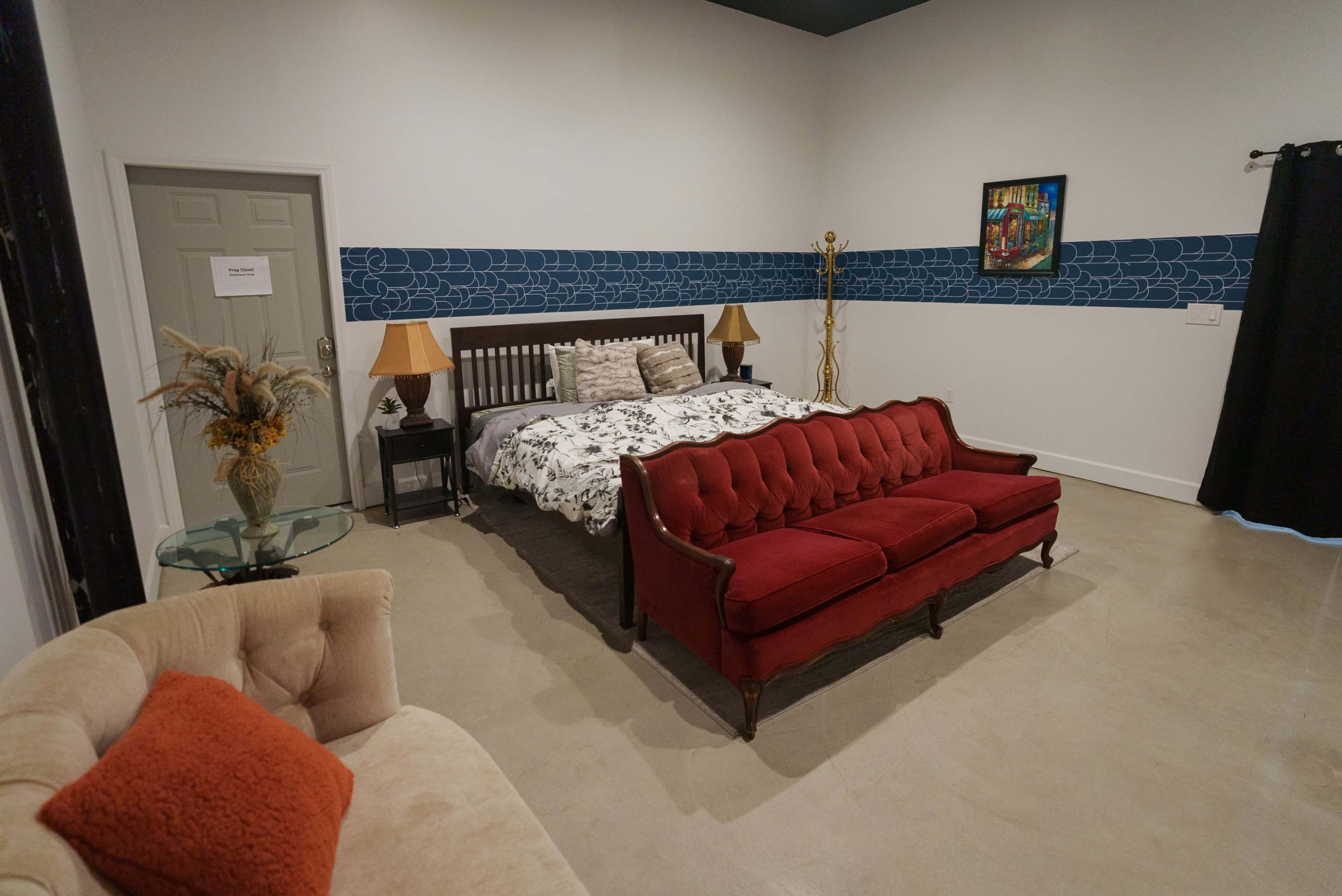 A spacious bedroom featuring a large bed with patterned bedding, a red vintage couch, and a decorative wall with a blue pattern.