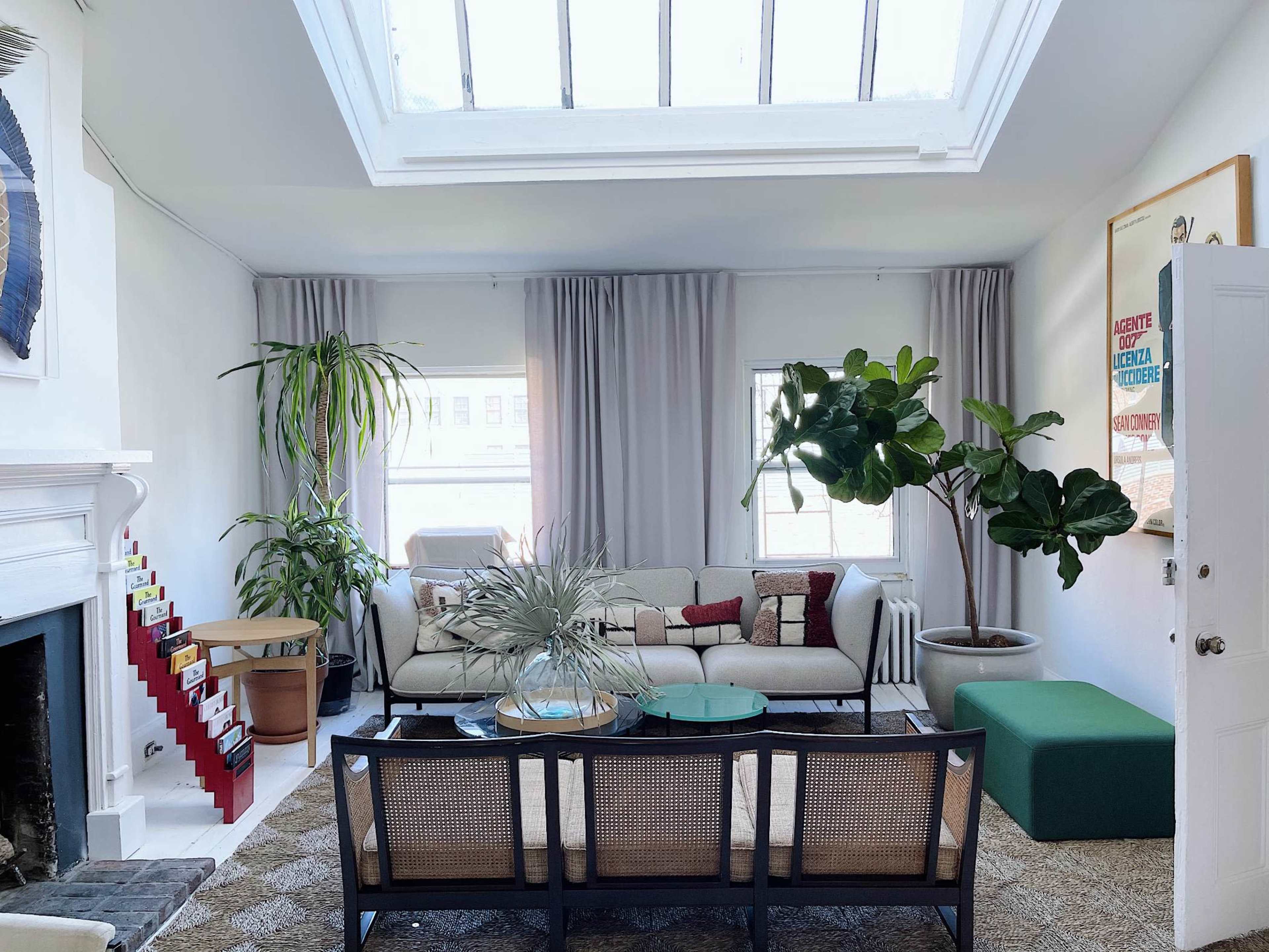 A modern living room featuring a sectional sofa, a coffee table, large windows with natural light, and indoor plants.