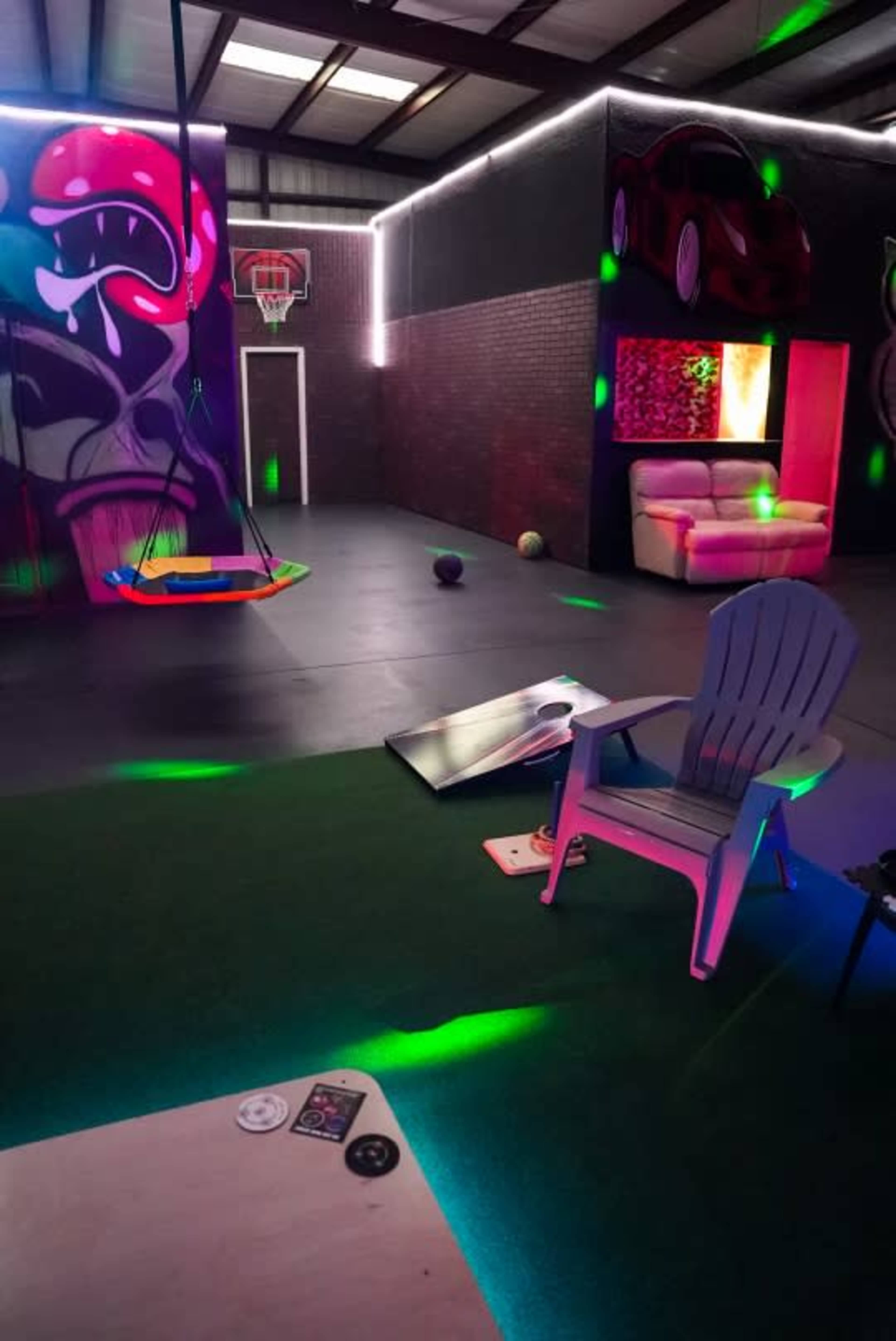 A recreational indoor space featuring a basketball hoop, a swing, colorful lighting effects, and a seating area with a couch.