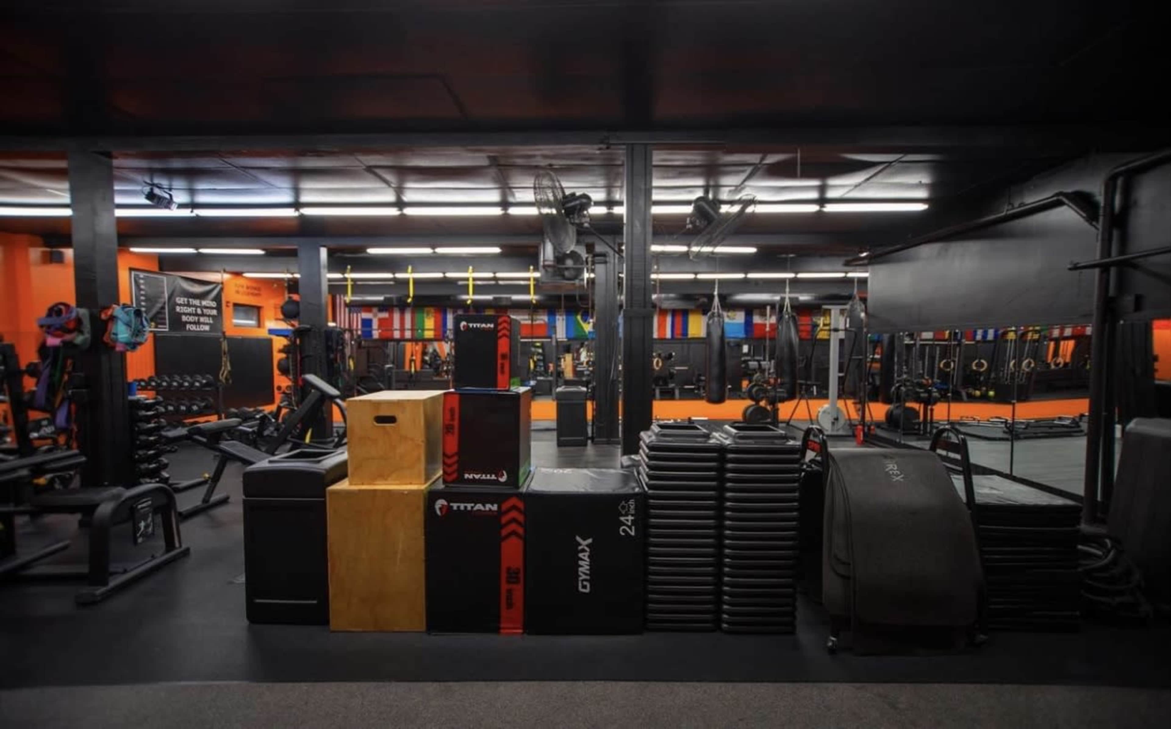 A modern gym interior with workout equipment, including stacked weights and boxes, arranged neatly against the walls.