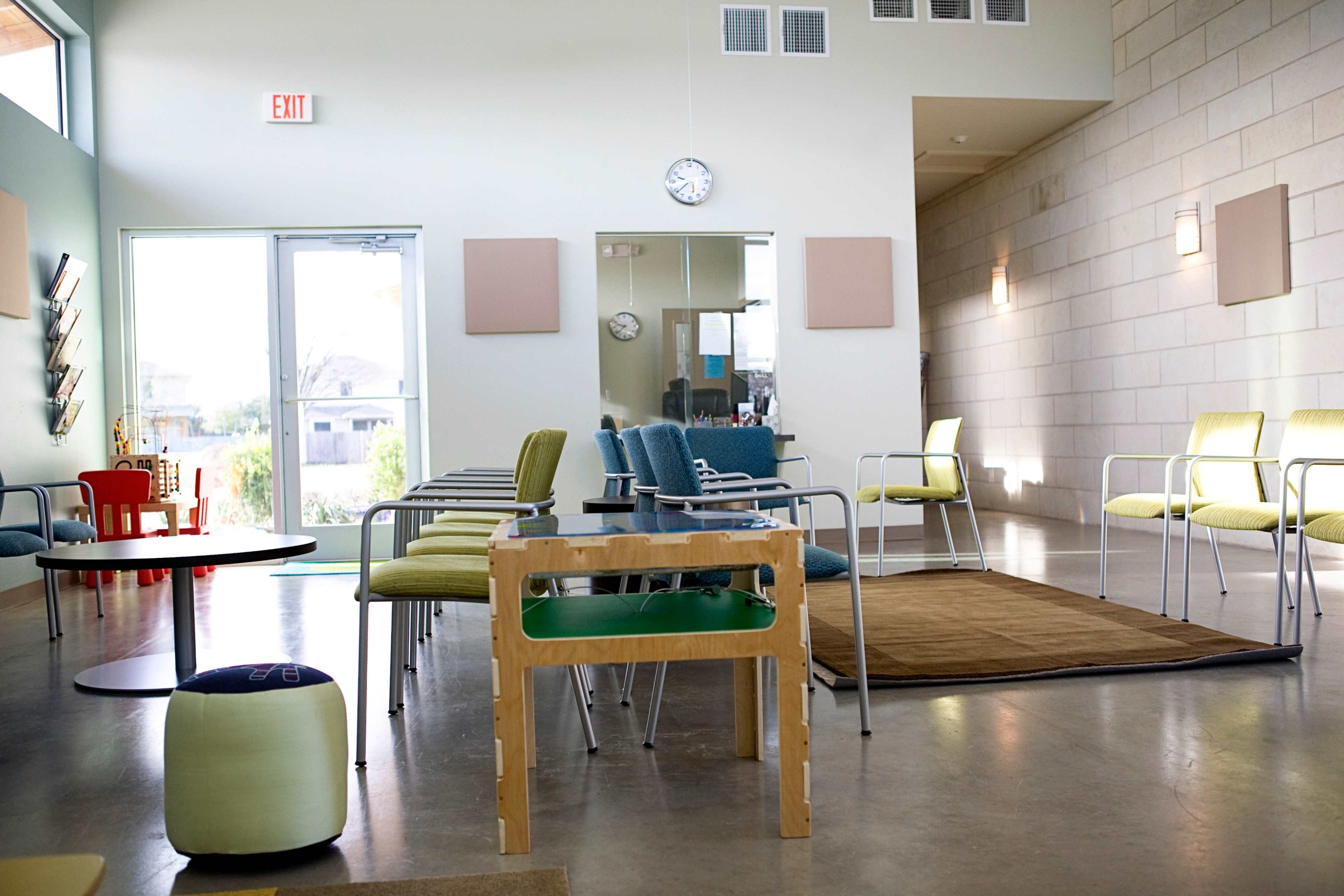 A bright waiting room with modern chairs arranged around a small table, featuring large windows that let in natural light.