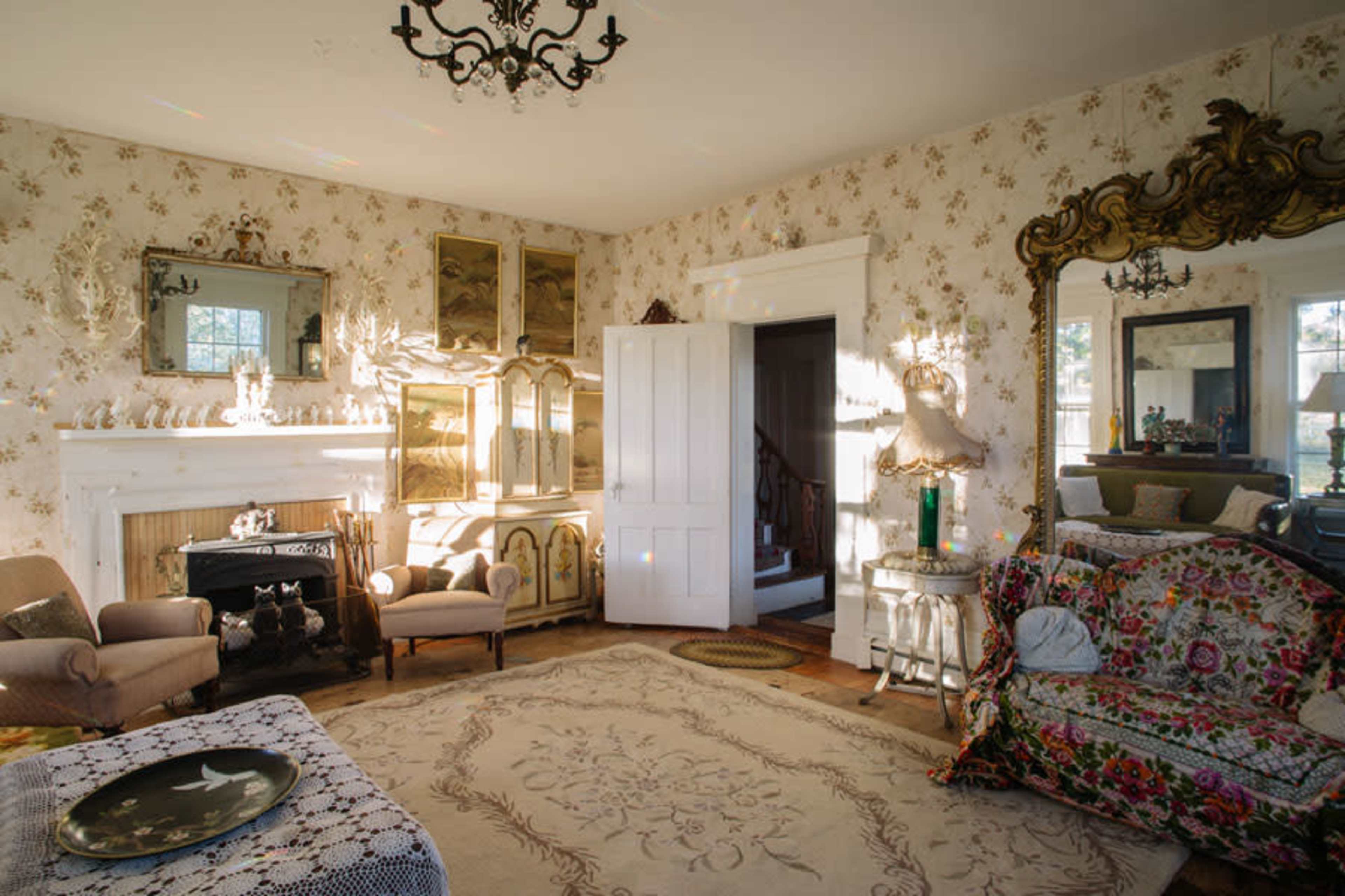 The room features vintage furniture, ornate mirrors, and floral wallpaper, illuminated by natural light from large windows.
