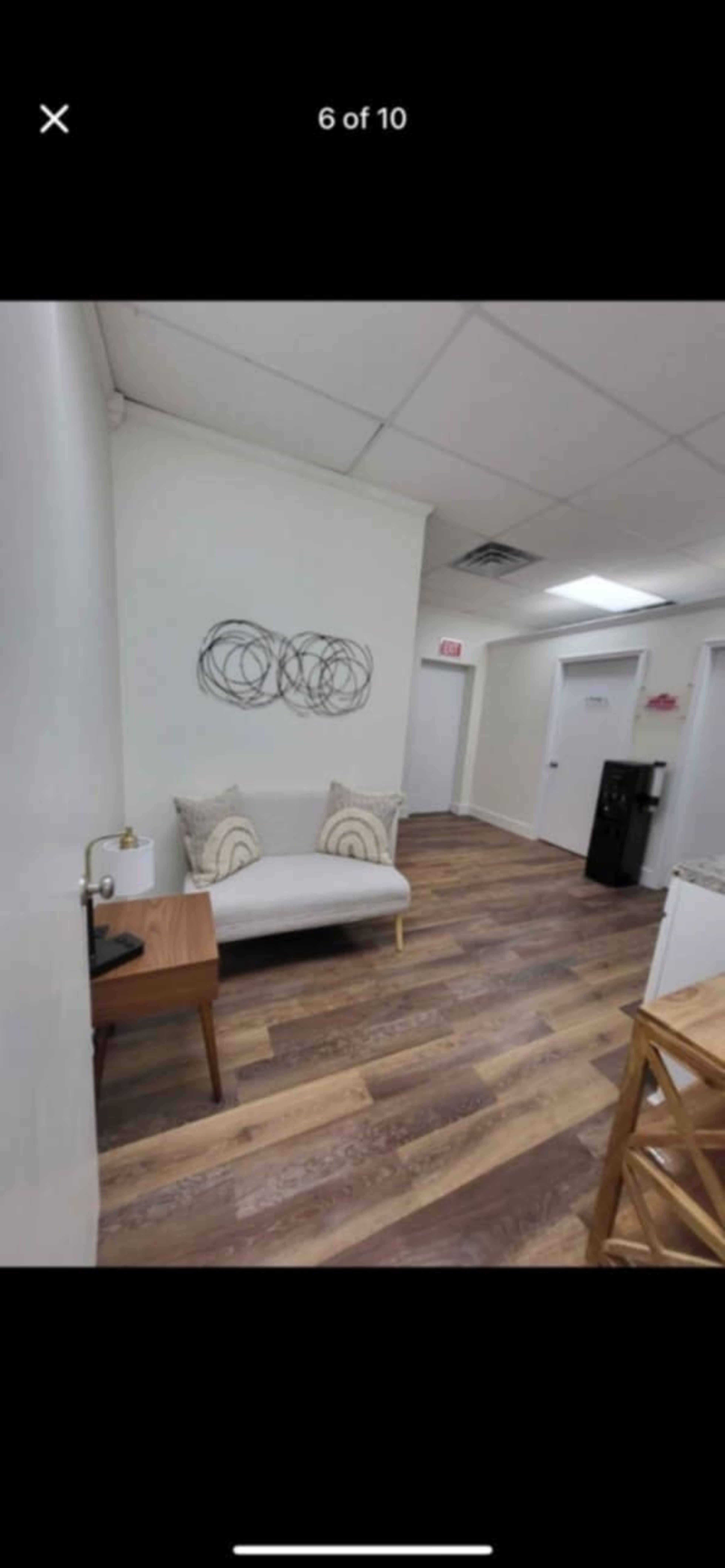 The image shows a well-lit office hallway with a couch, a wooden side table, and light-colored walls.