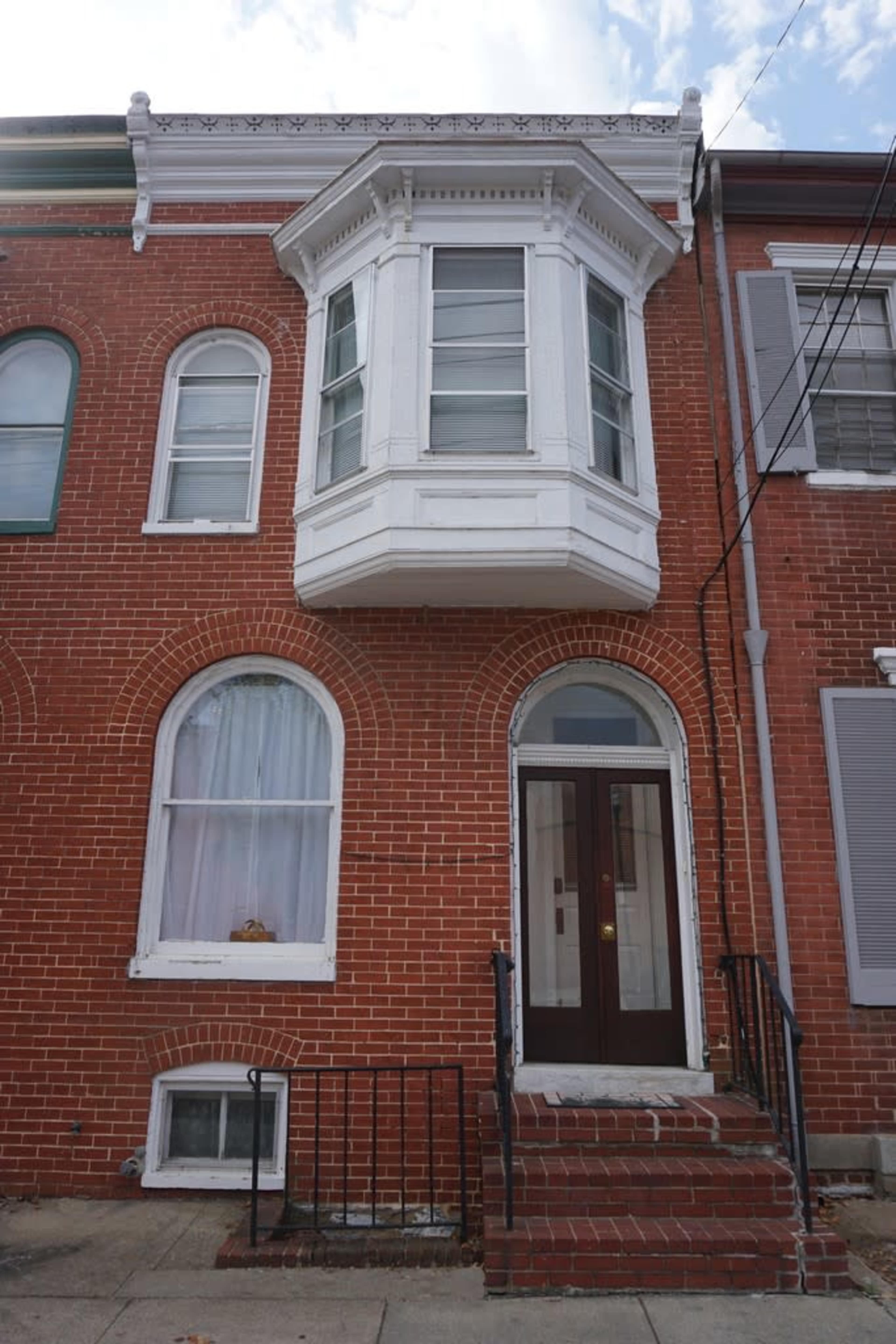 A brick townhouse featuring a large bay window on the second floor and a simple entryway with steps leading up to the front door.