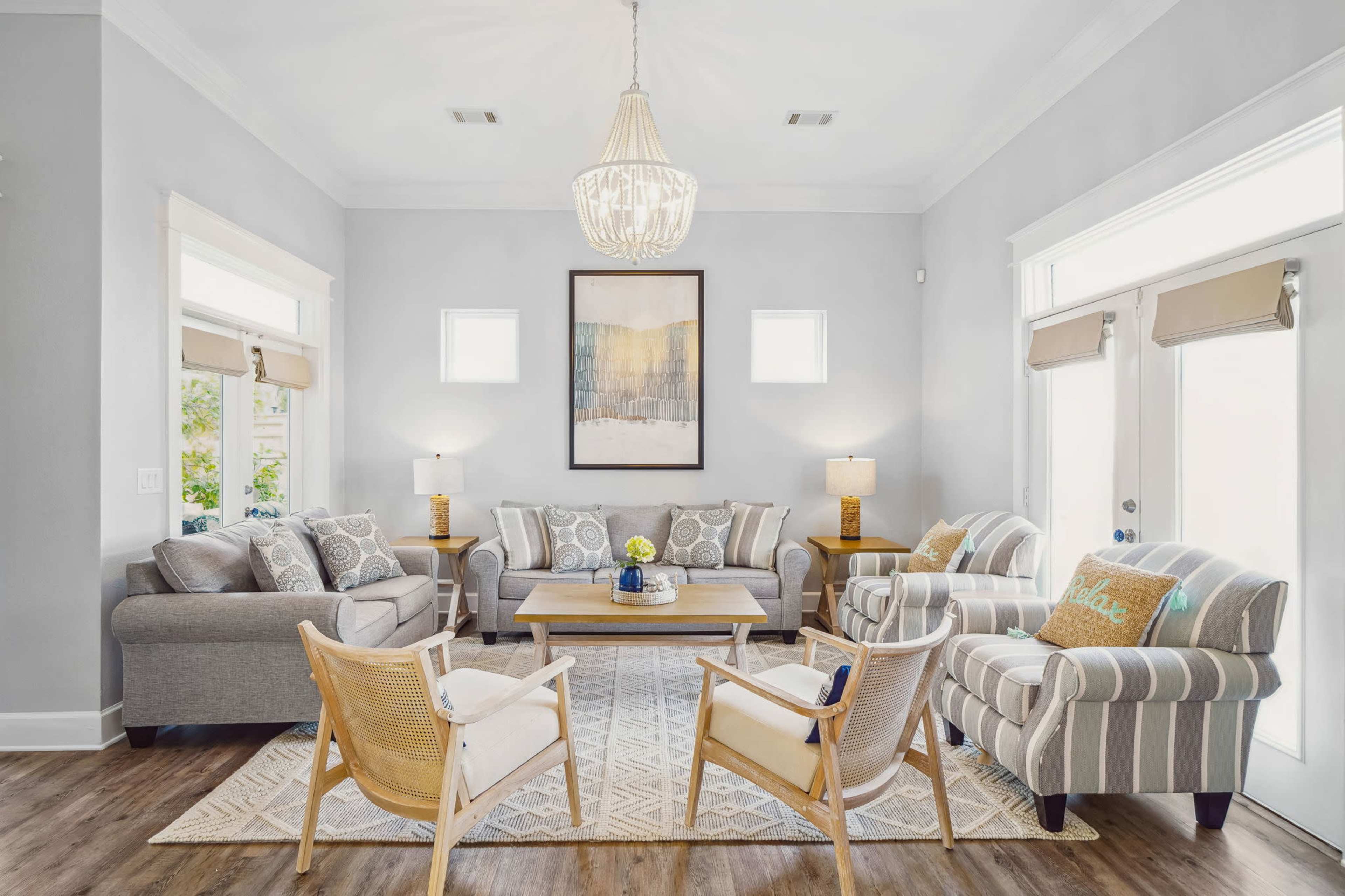 A bright living room features two sofas, two armchairs, a coffee table, and a large wall art piece with light-colored walls and natural light streaming through the windows.