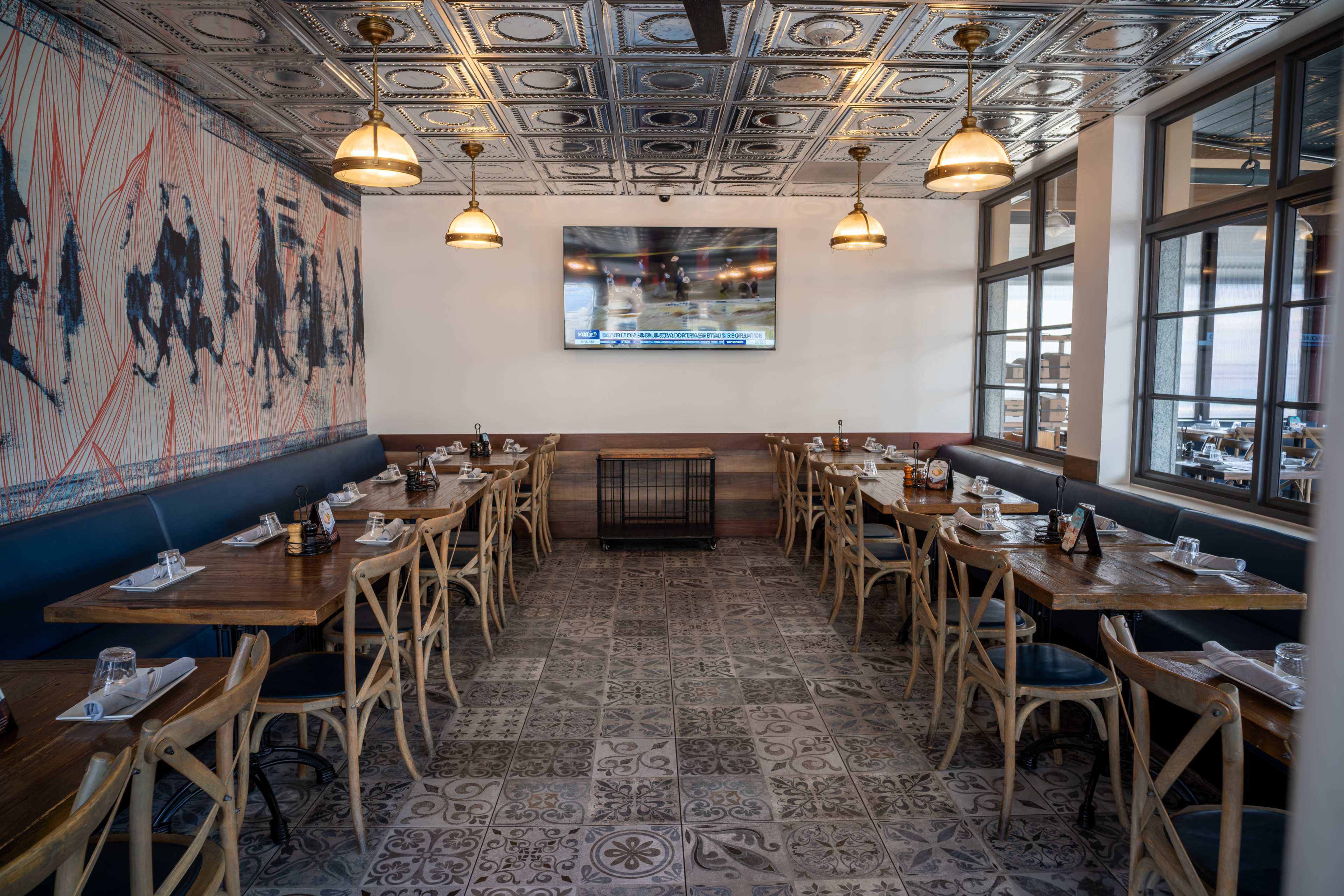 The image shows a spacious restaurant interior featuring wooden tables and chairs, a decorative ceiling, and a large television mounted on the wall.